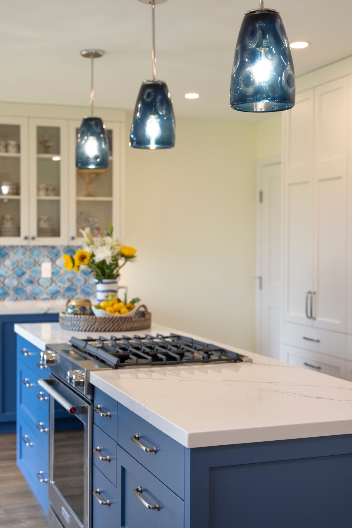 Kitchen with blue cabinets, white countertop, hanging blue pendant lights, and a vase of flowers on the island.