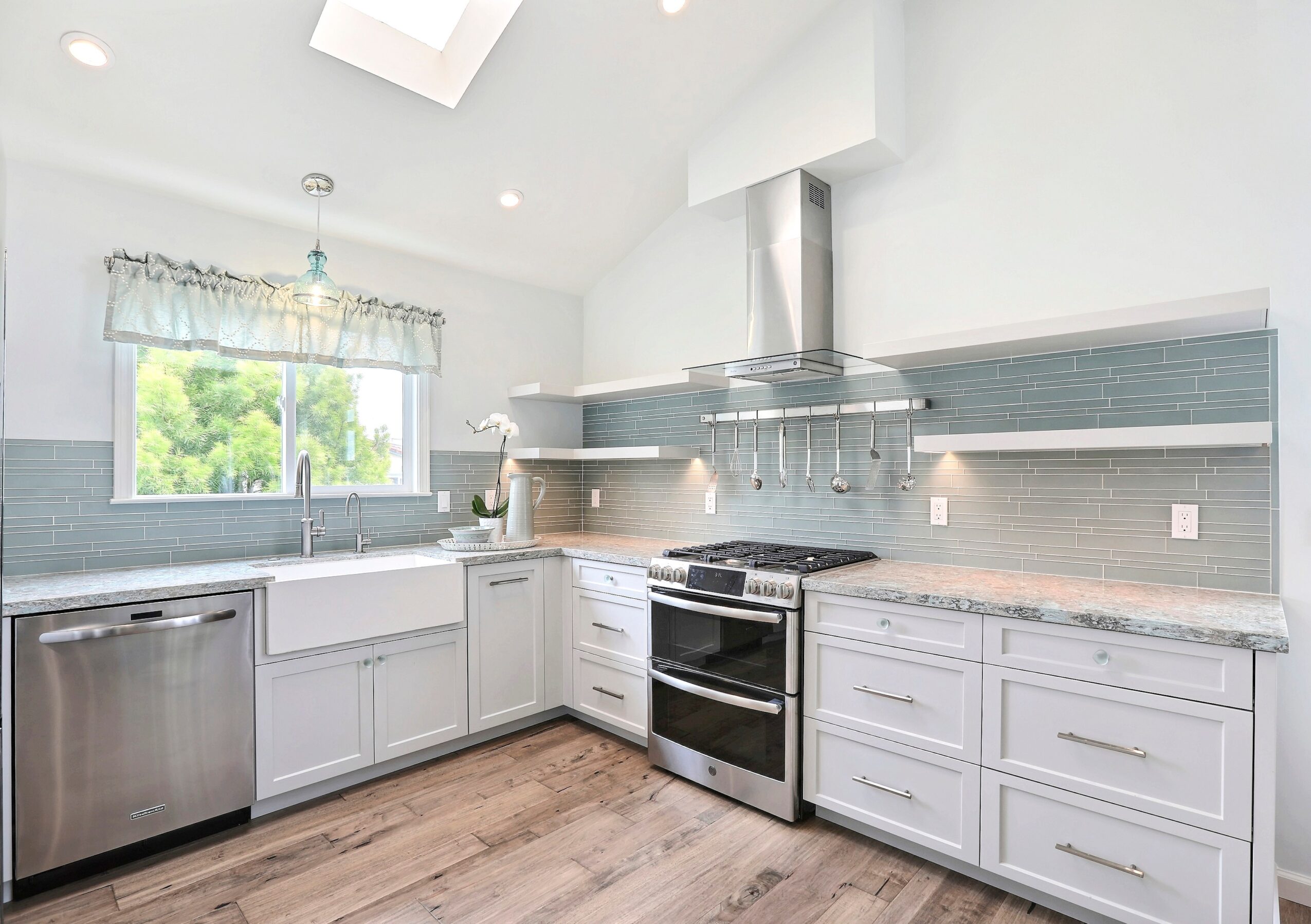 Bright kitchen with white cabinets, stainless steel appliances, a window with a valance, and a modern backsplash.