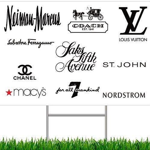 Signboard displaying luxury brand logos and store names, with green grass at the bottom.