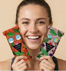 Woman smiling holding colorful, patterned face masks with cartoon faces, against a beige background.
