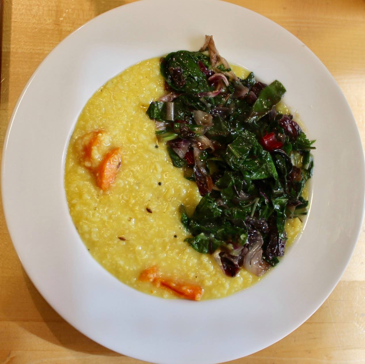 Plate with yellow polenta and a side of mixed greens salad with cherry tomatoes, on a wooden table.