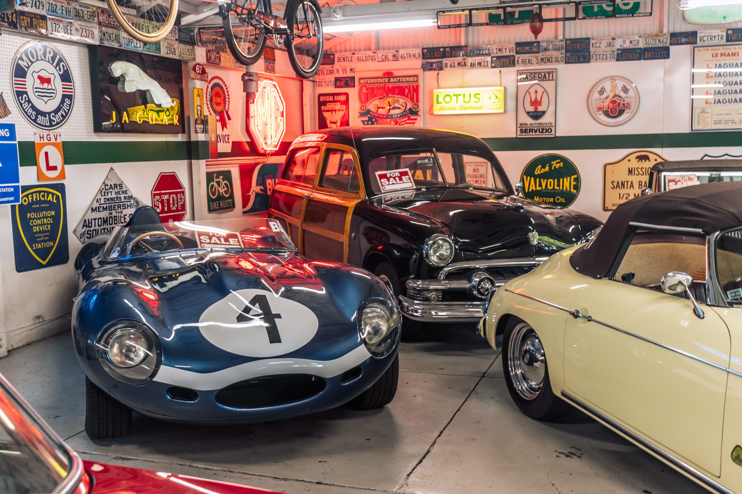 Three vintage cars parked indoors with various signs and posters on the wall behind them.