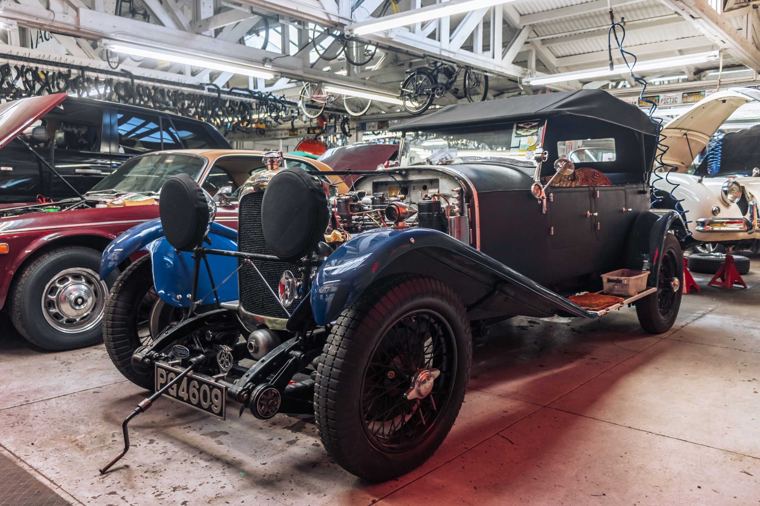 Vintage black car with large wheels and open top, displayed indoors among other classic vehicles.