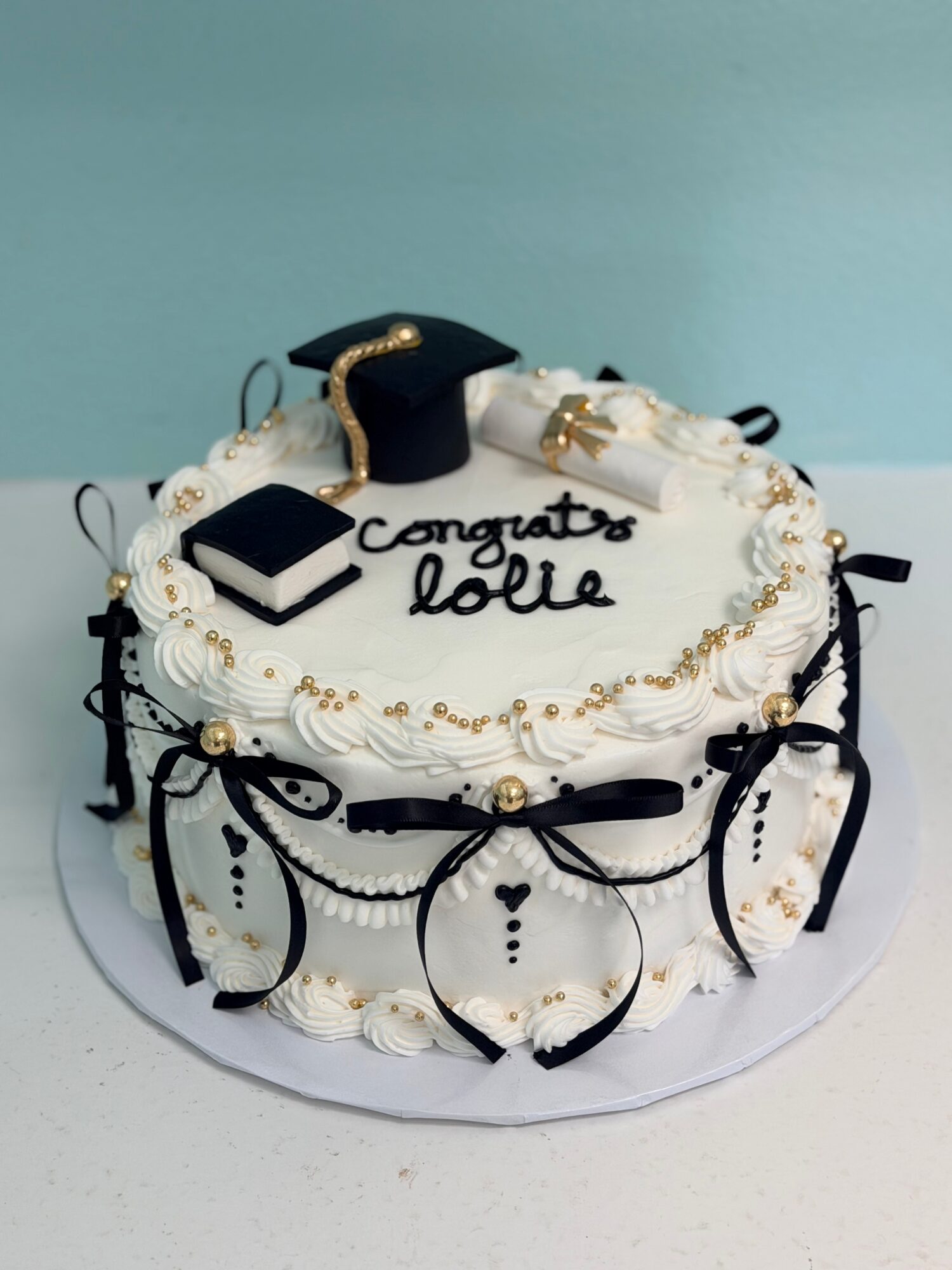 Round cake with white frosting, black and gold decorations, graduation cap, and a message saying 'congrats jolie'.