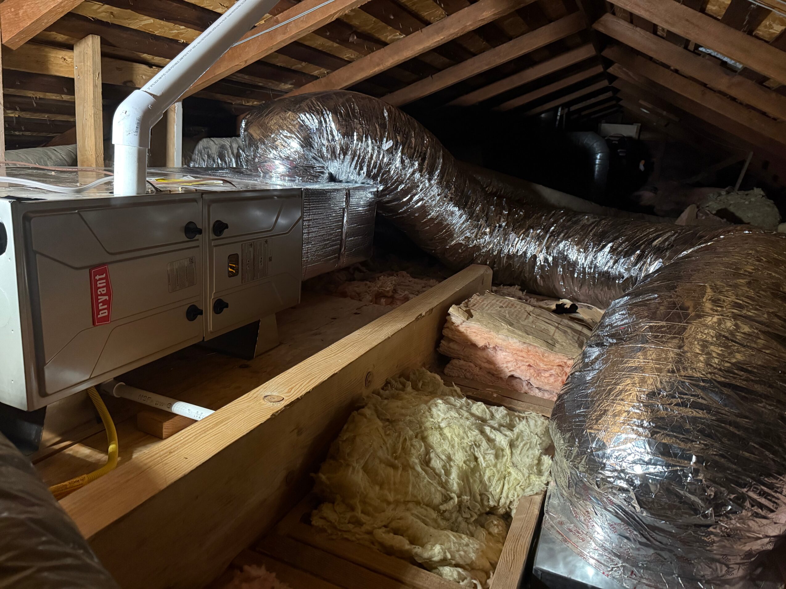 Insulation, ductwork, and HVAC system components in an attic space with wooden beams.