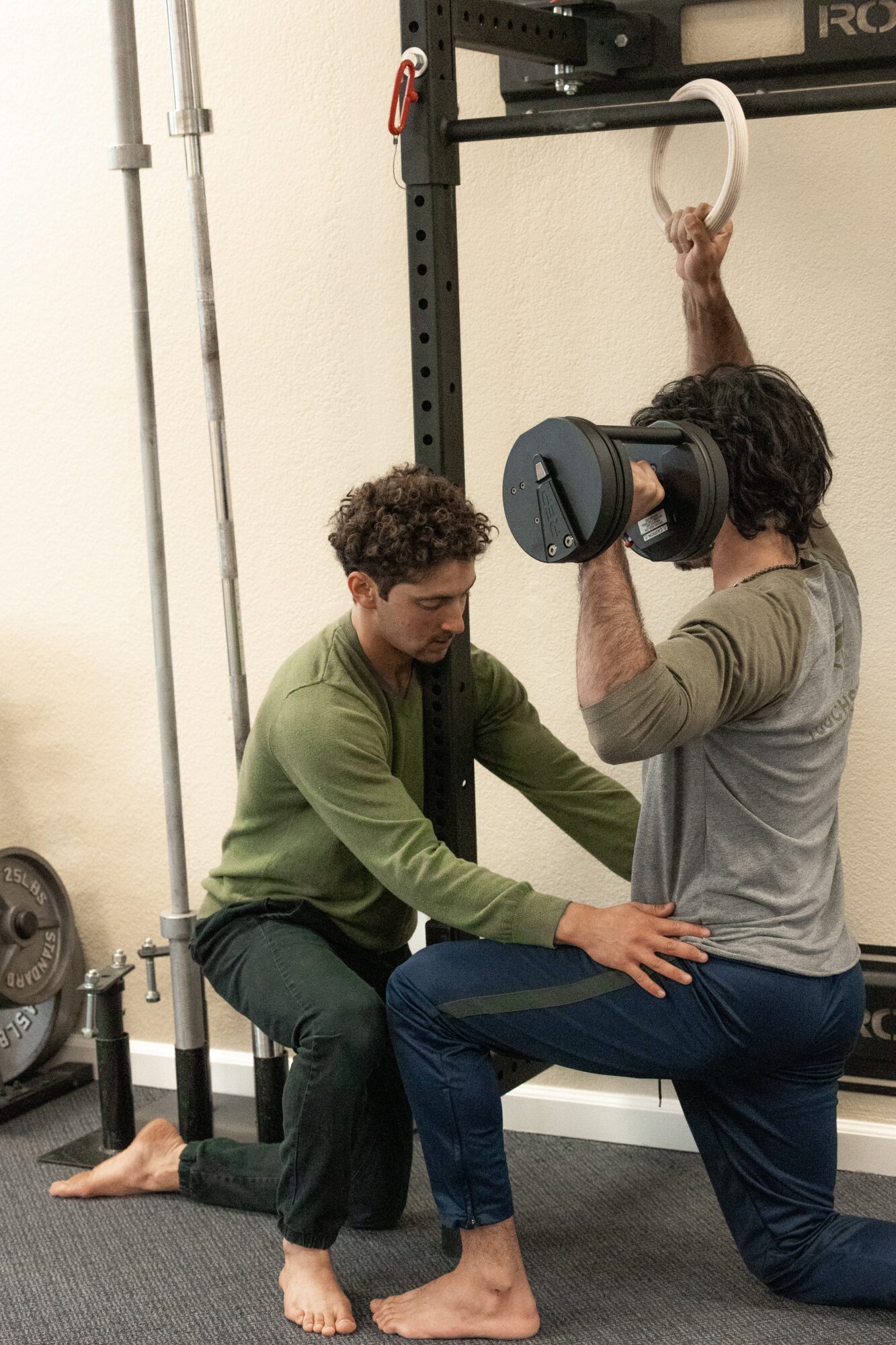 Person holding a weight plate while another person supports them during a workout in a gym.