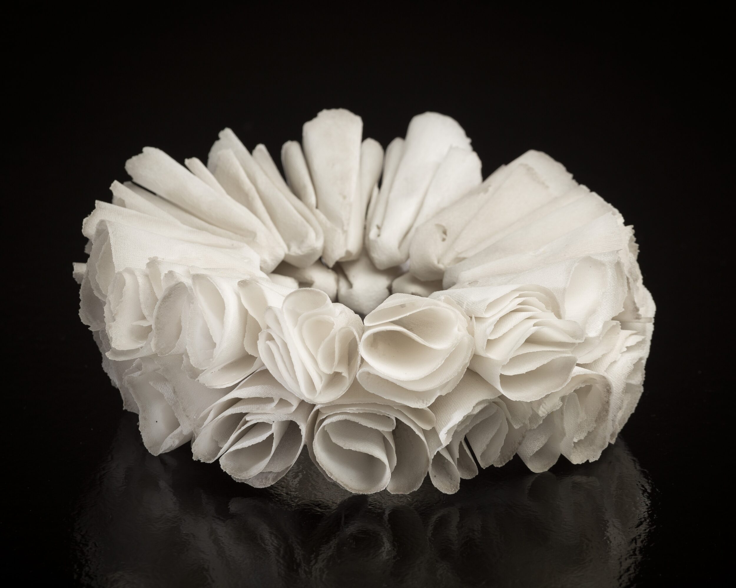 White decorative ring made of fabric or paper flowers on black background.