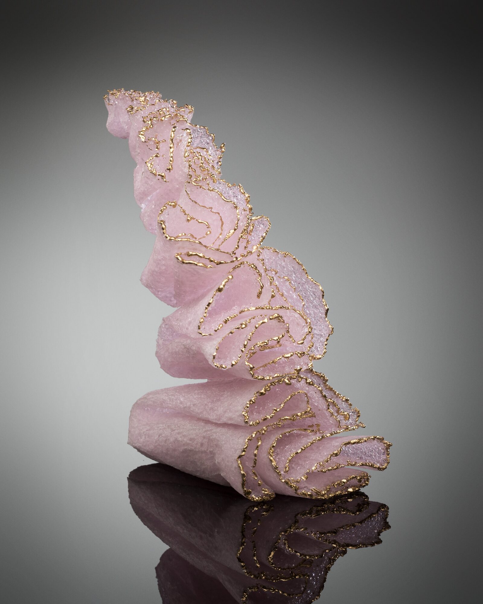 Pink towel with gold embellishments, rolled and standing upright, reflected on a glossy surface.