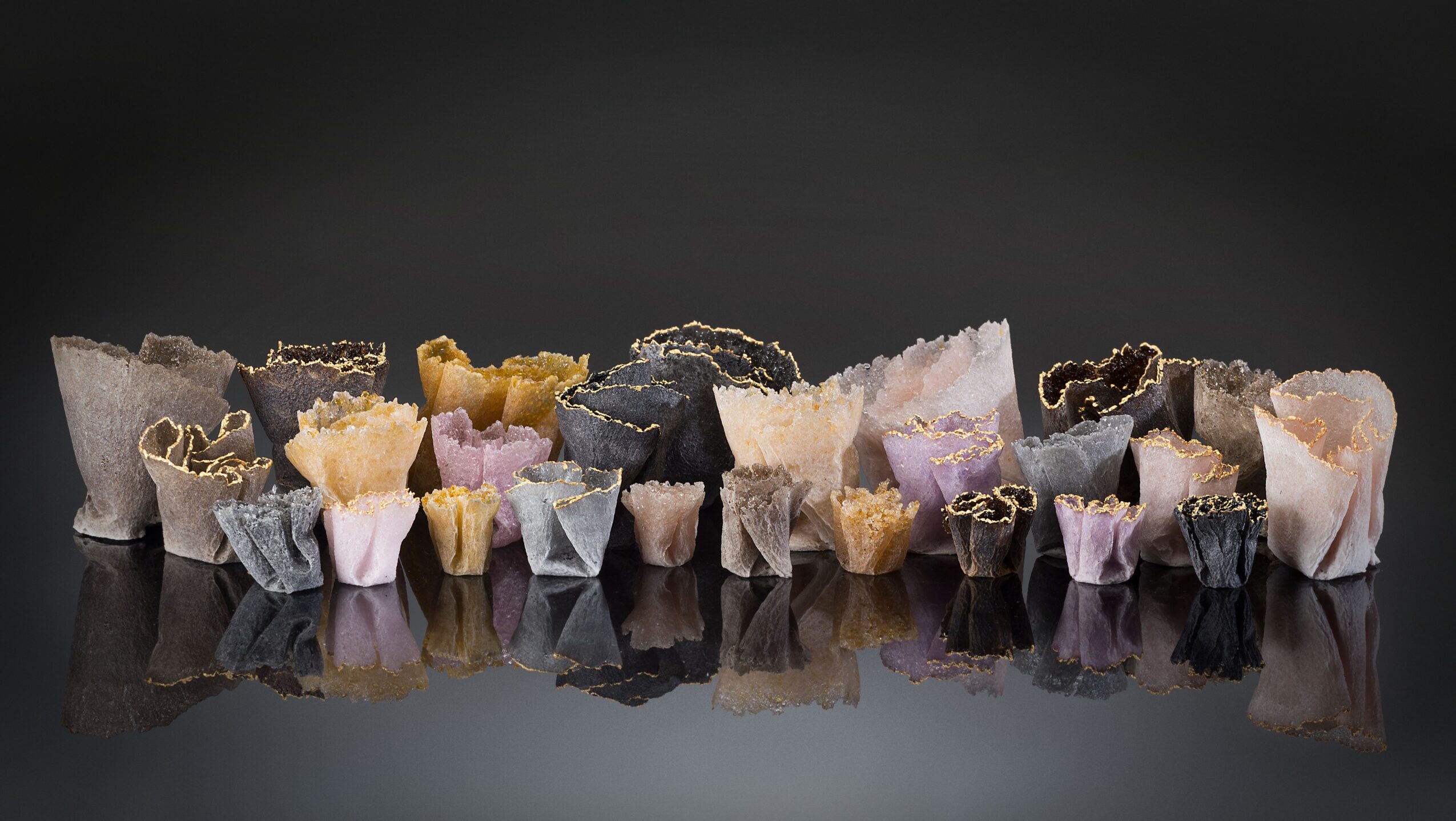 Various colorful candies wrapped in paper, arranged in a row on a reflective surface, with a dark background.