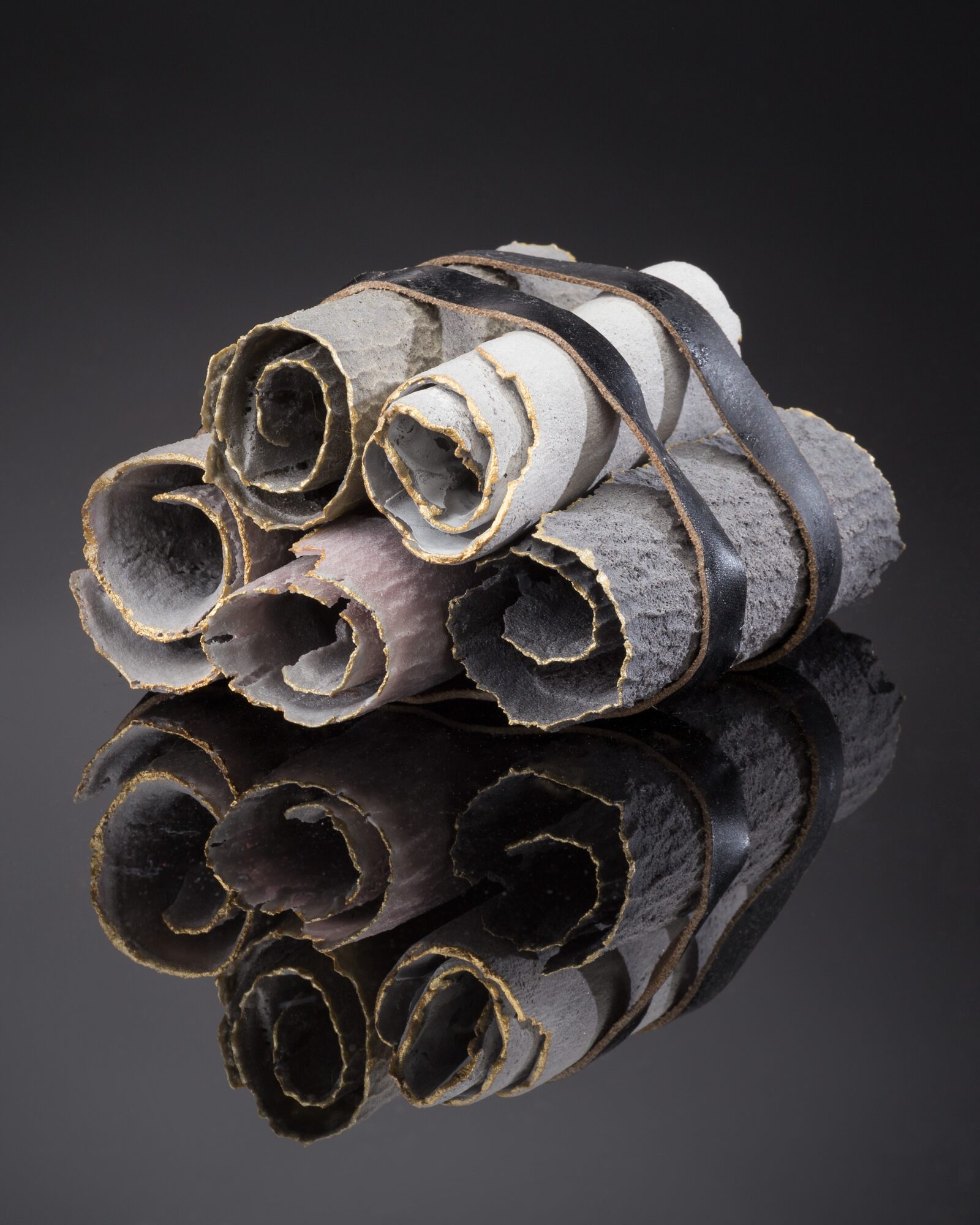 A bundle of rolled paper tied with a rubber band, reflected on a glossy black surface.