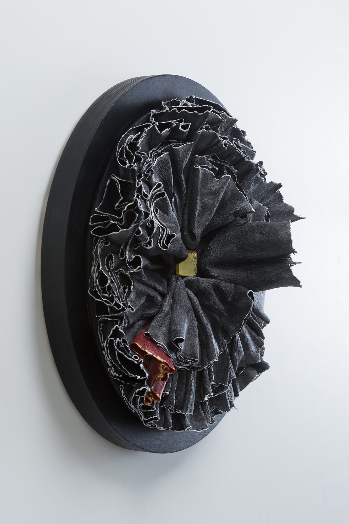 Black fabric scrunchie with ruffles on a black circular base, viewed from the side.
