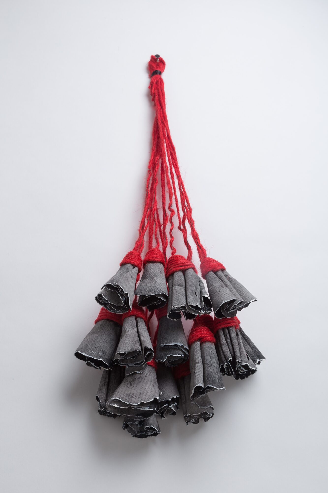Cluster of small gray fabric bells hanging from red strings against a white background.