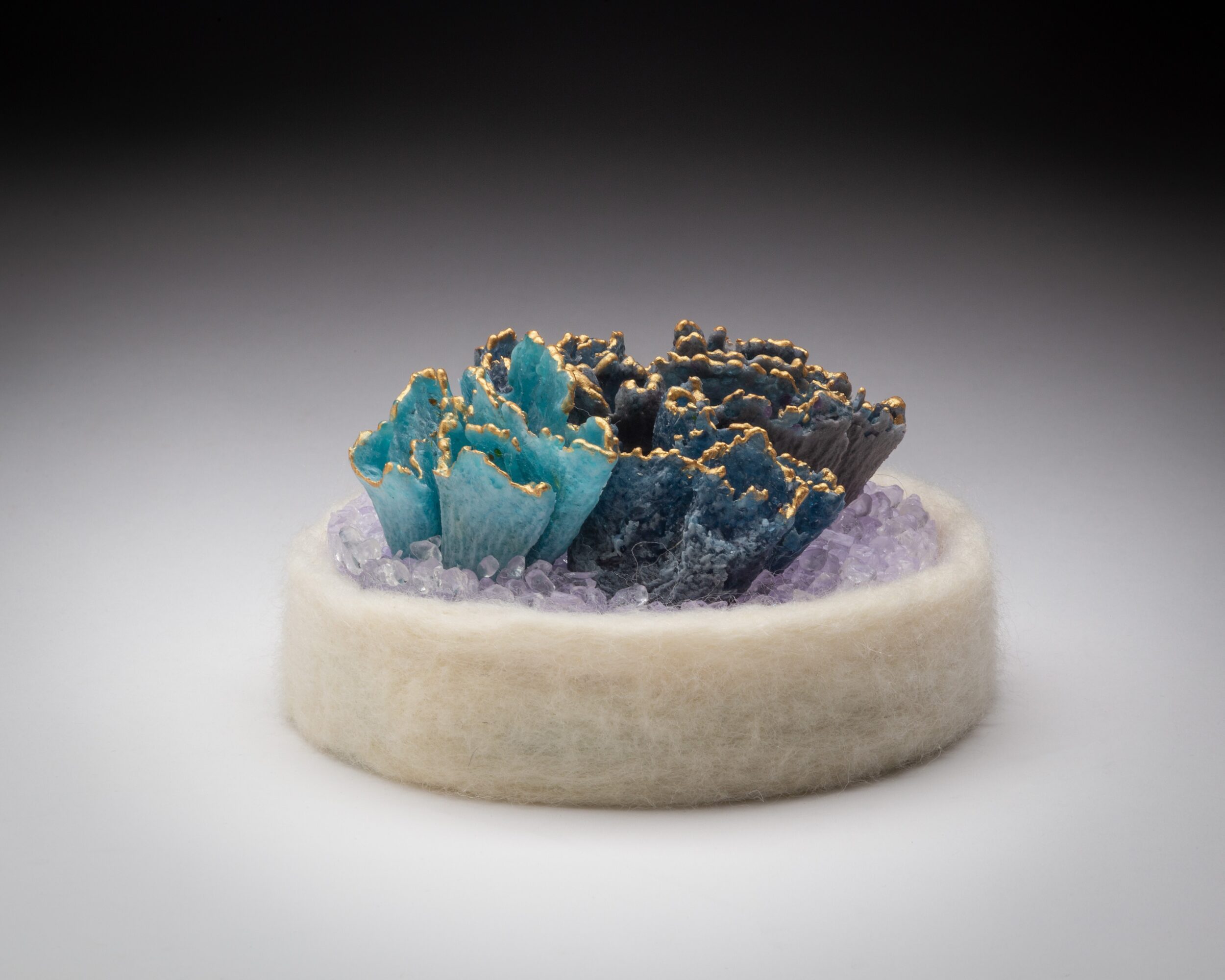 Close-up of a small, textured sculpture with blue and dark gray colors on a white circular base.