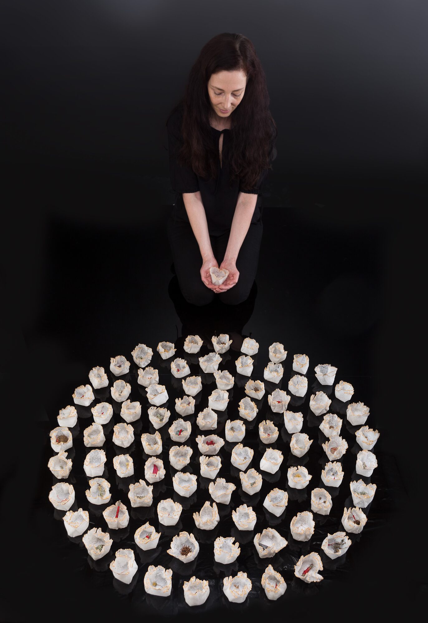 Woman with long dark hair looking down at a circular arrangement of small white objects on a black surface.