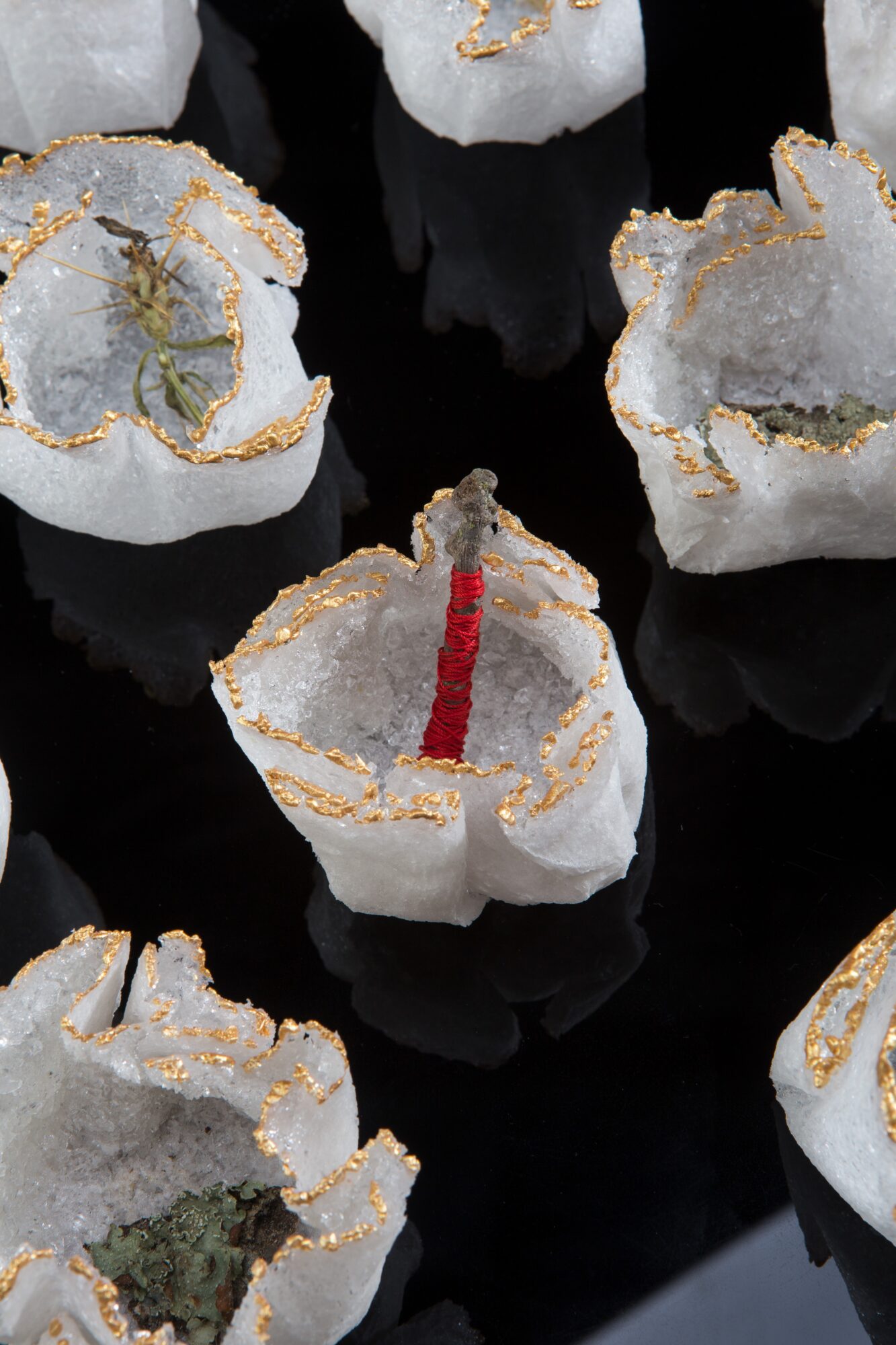 Several white candles with gold accents, one with a red wick, on a black reflective surface.