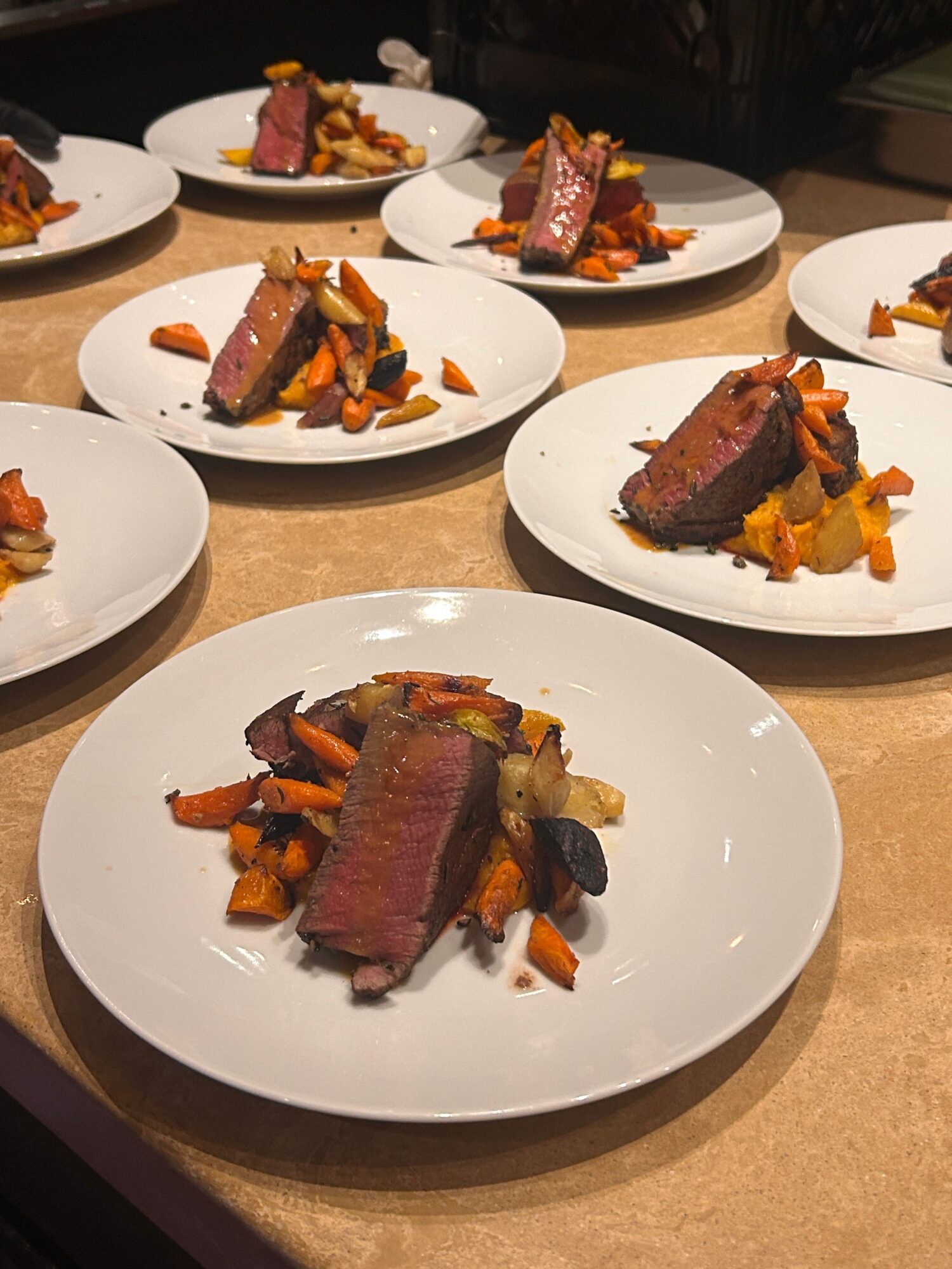 Slices of cooked meat with roasted vegetables on white plates, arranged on a table.