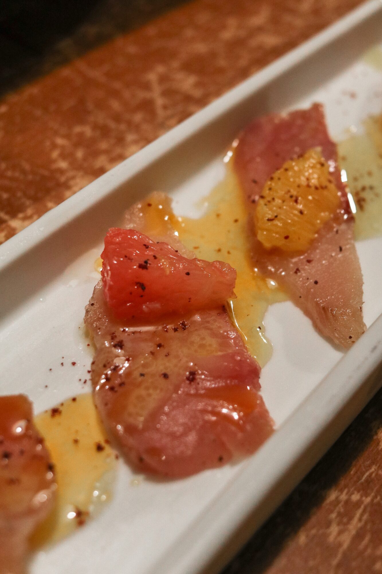 Slices of raw fish topped with orange and yellow garnishes on a white plate, with some oil or sauce drizzled.