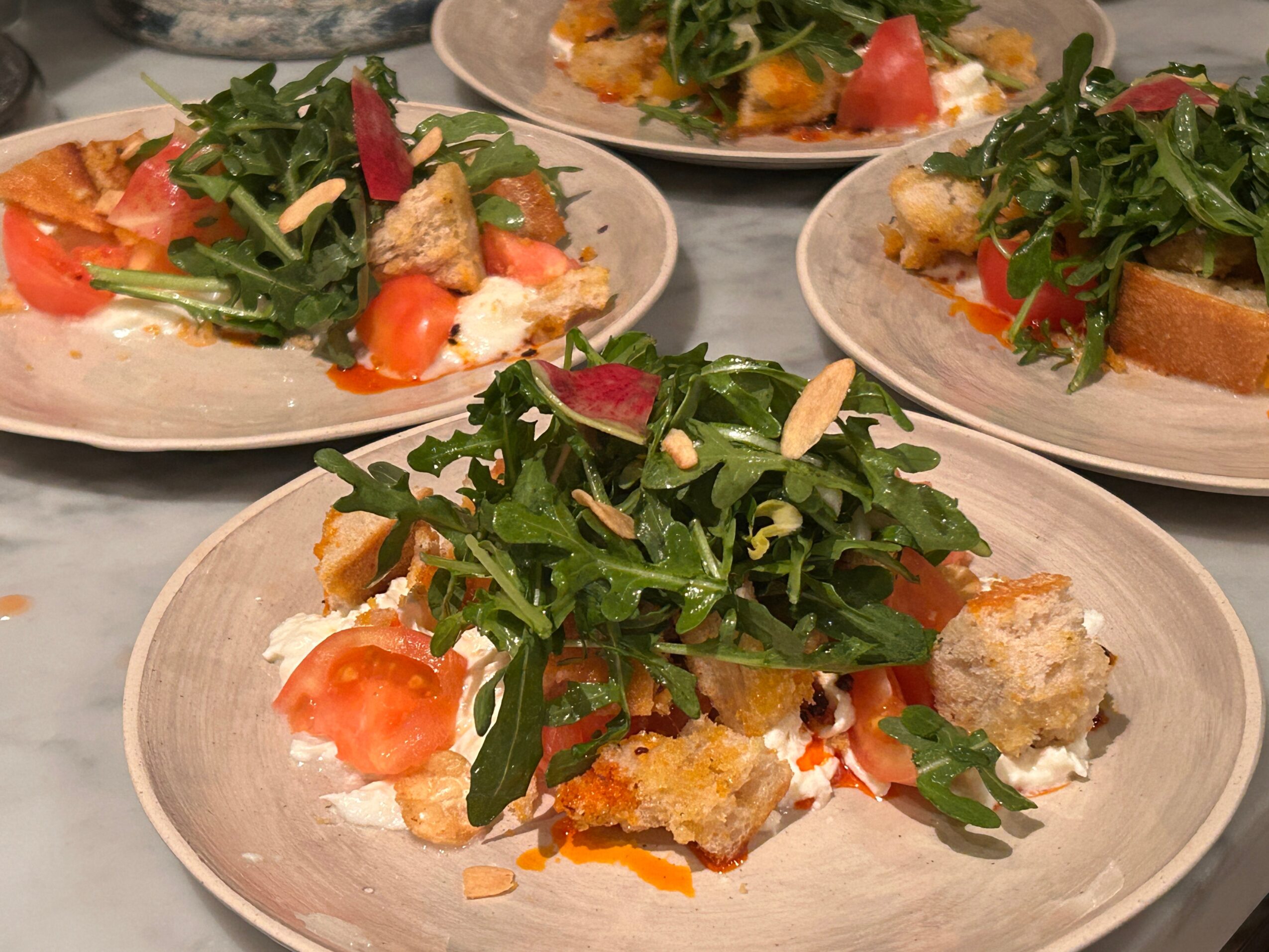 Three plates with salads containing greens, tomatoes, and breaded items on a table.
