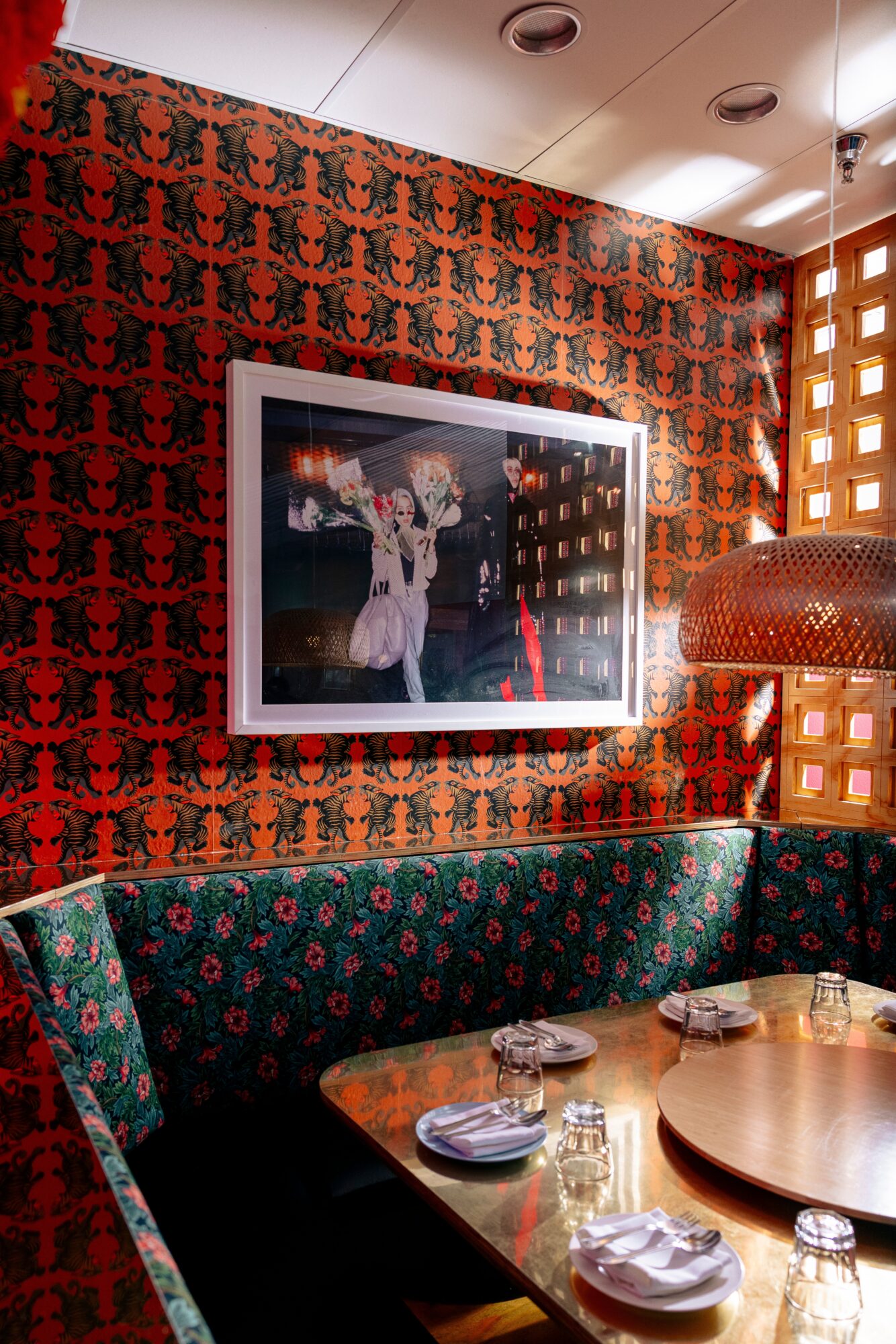 Interior of a restaurant with patterned wallpaper, a framed photo on the wall, and a table set with plates and glasses.