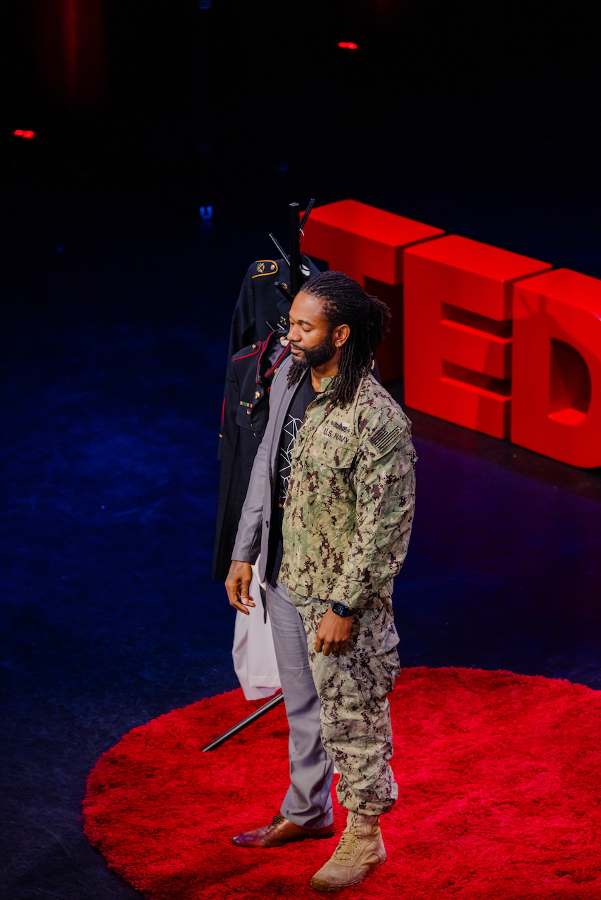 Two people standing on a red circular carpet with a large red TED logo behind them, in a dark setting.