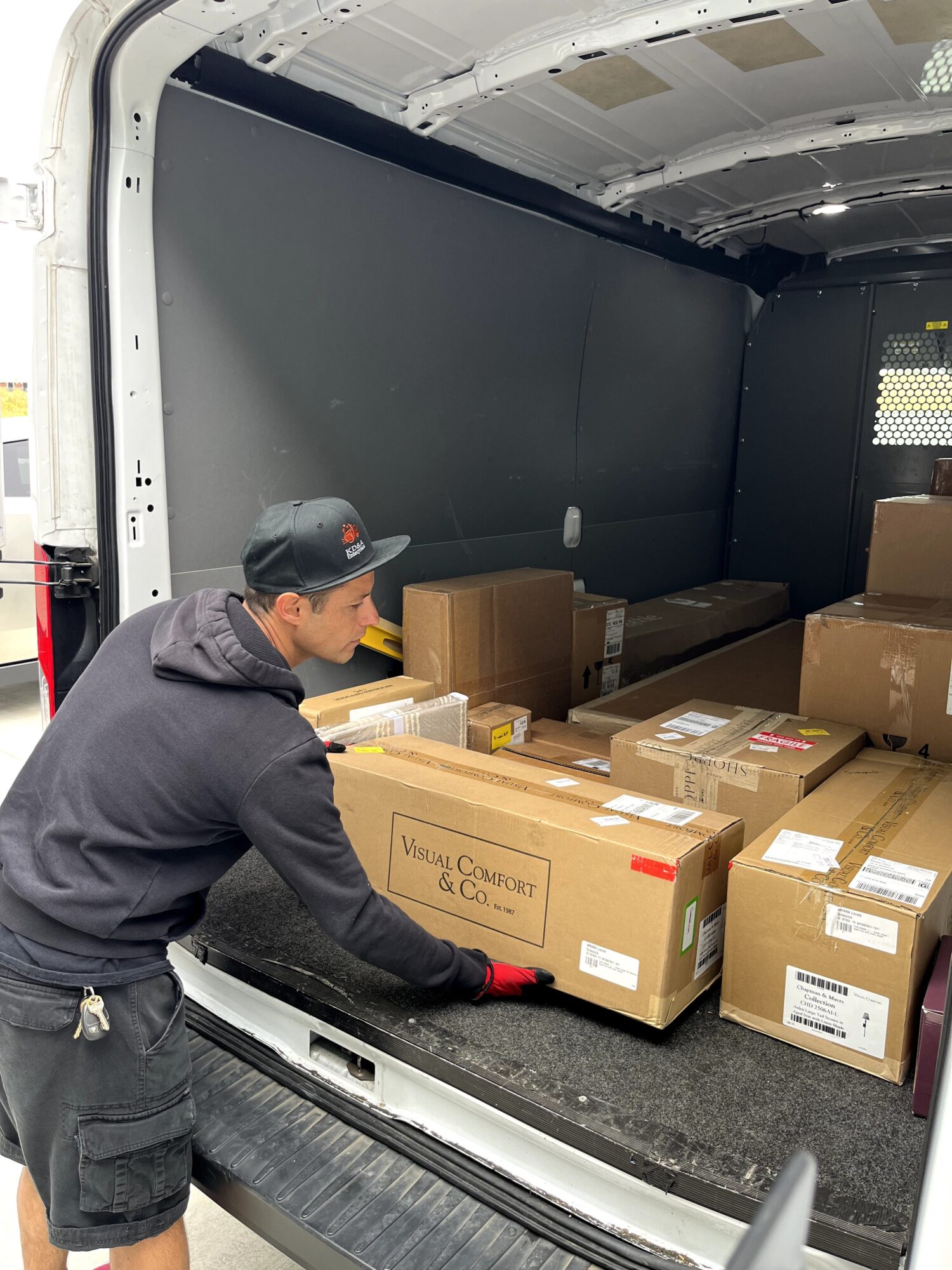 Man loading boxes into a van, with boxes stacked inside, some labeled, in a cargo area with black interior walls.