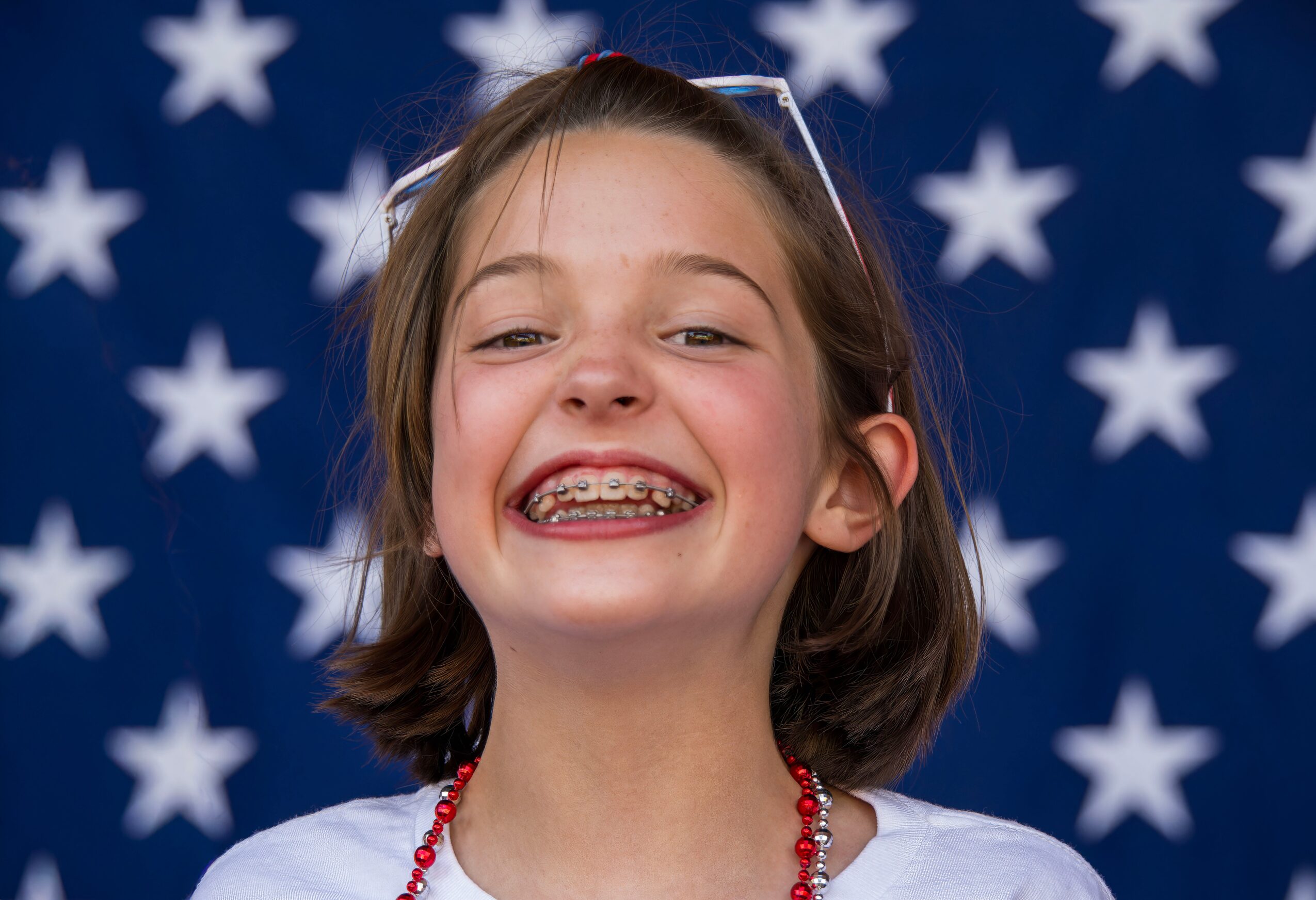Young girl with braces smiling, background with white stars on a blue field.