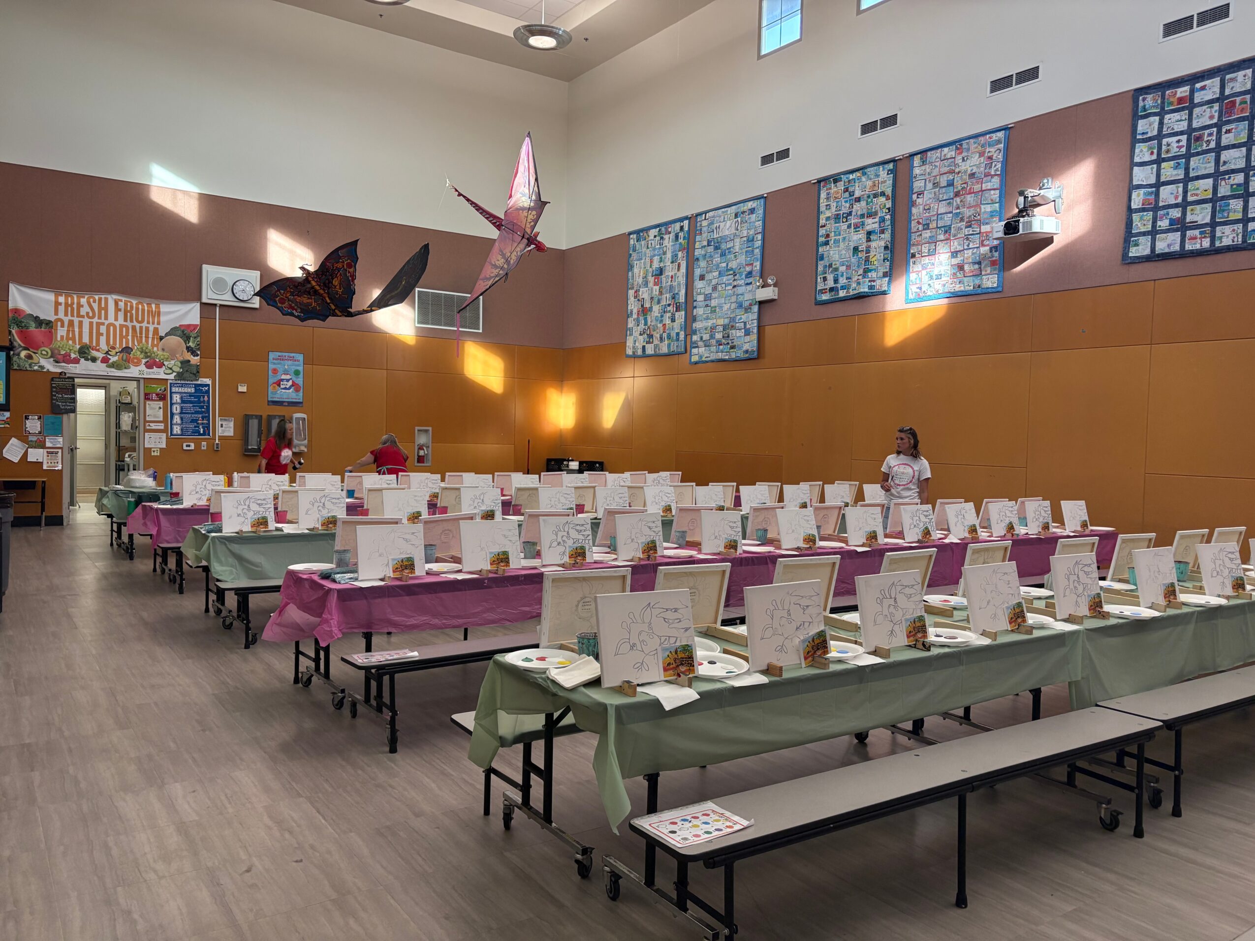 Large room with long tables covered in pink and green tablecloths, set with plates and cups, and a person standing at the back.