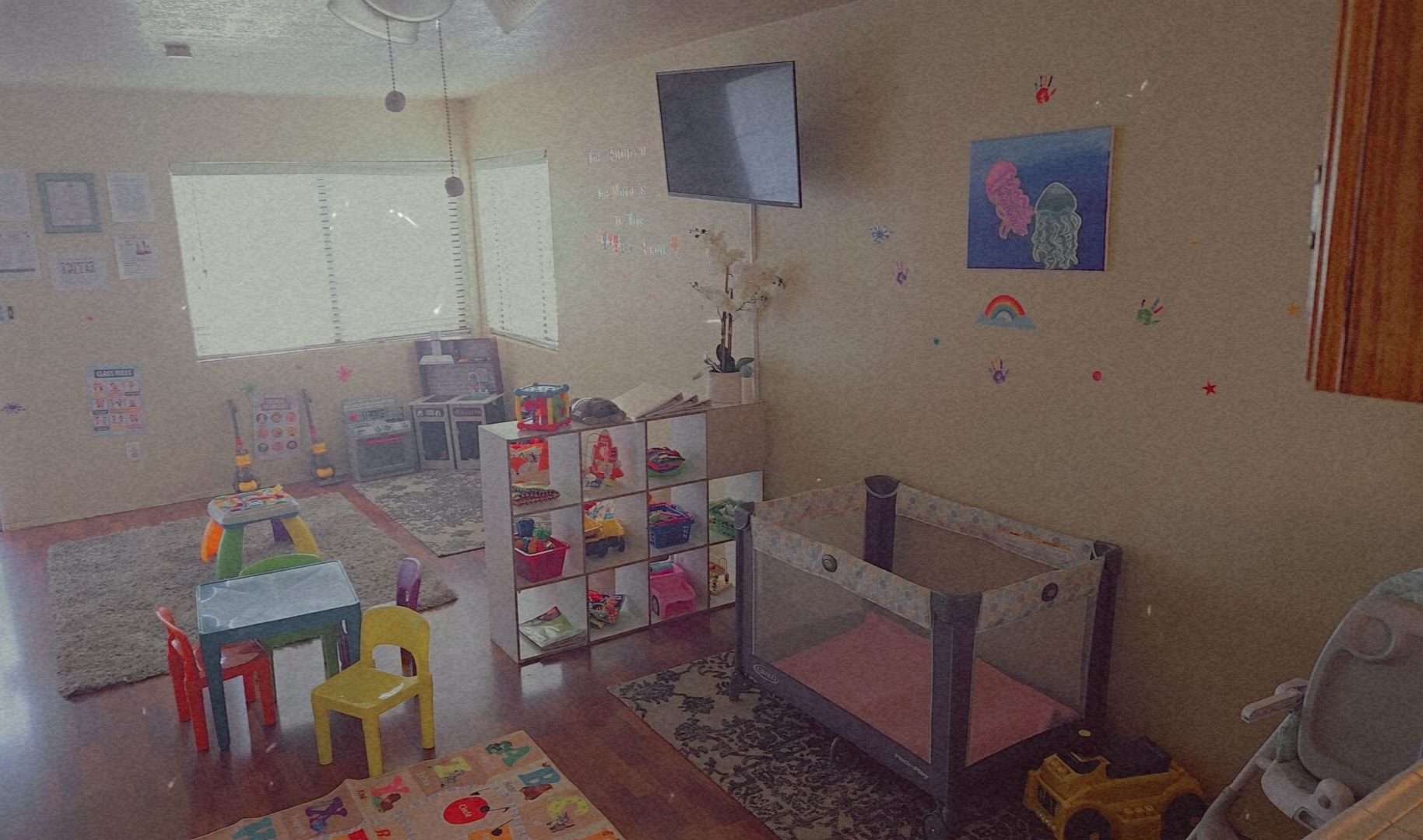 Children's playroom with toys, furniture, and a television on the wall.