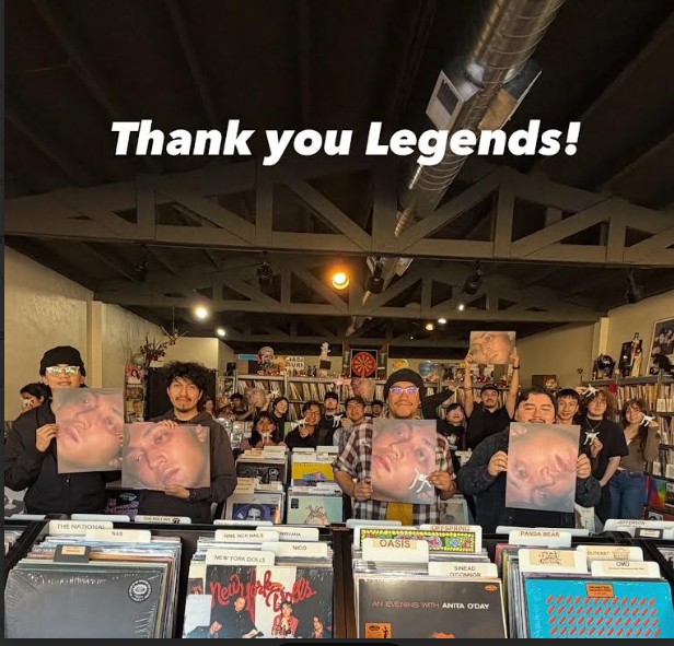 Group of people holding vinyl records inside a store, with shelves and posters in the background, and text saying 'Thank you Legends!'