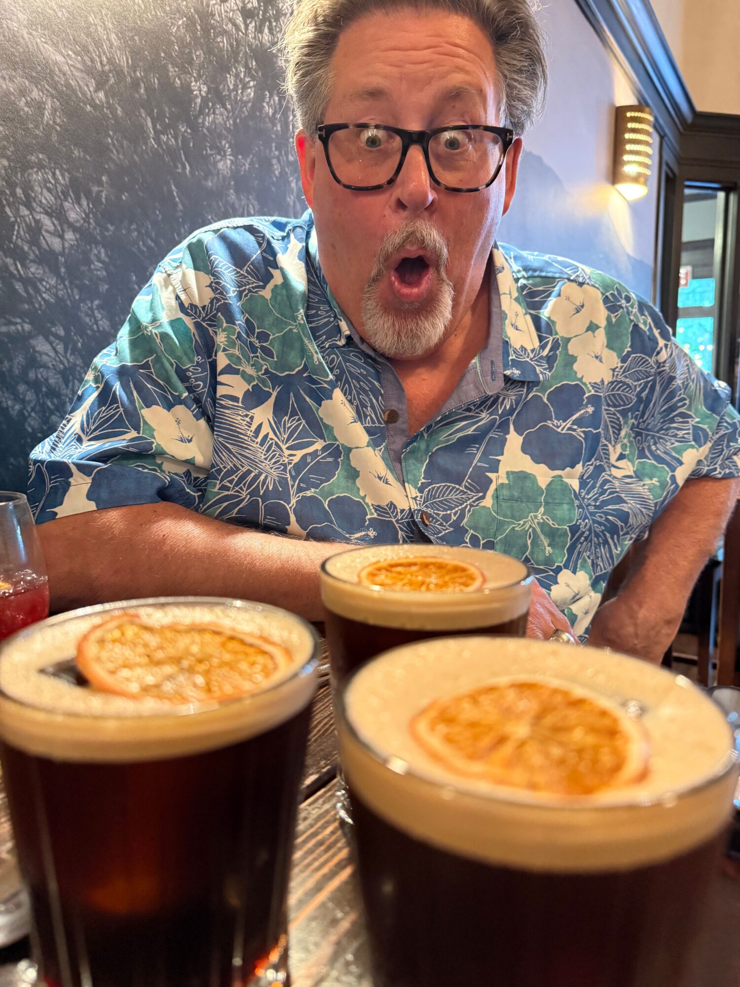 Man with glasses and a floral shirt surprised at a table with three bowls of food.