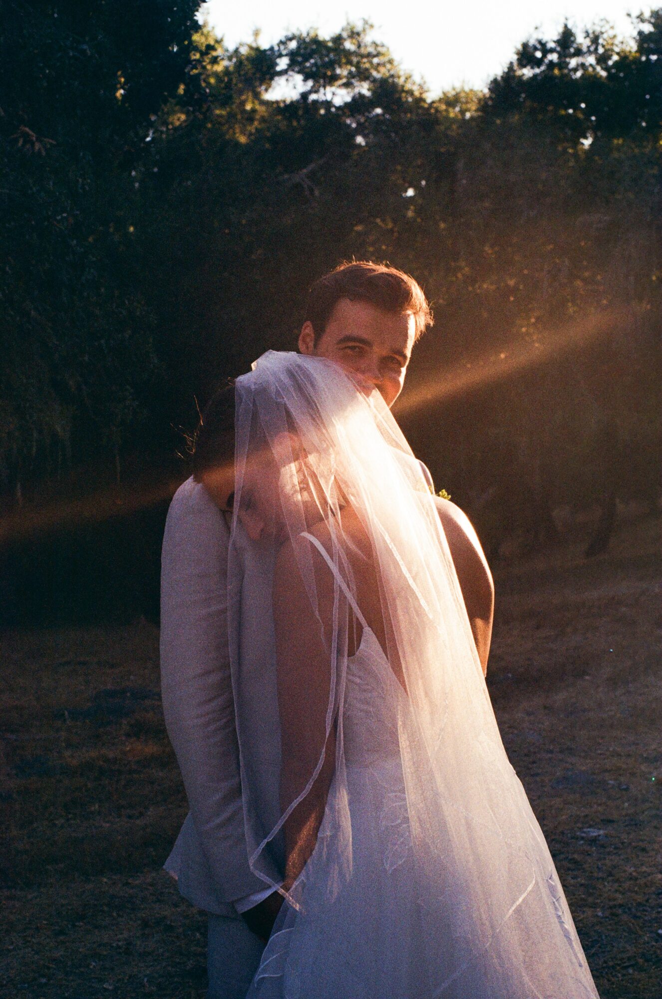 Person with a veil on their head, standing outdoors during sunset, with sunlight shining behind them.