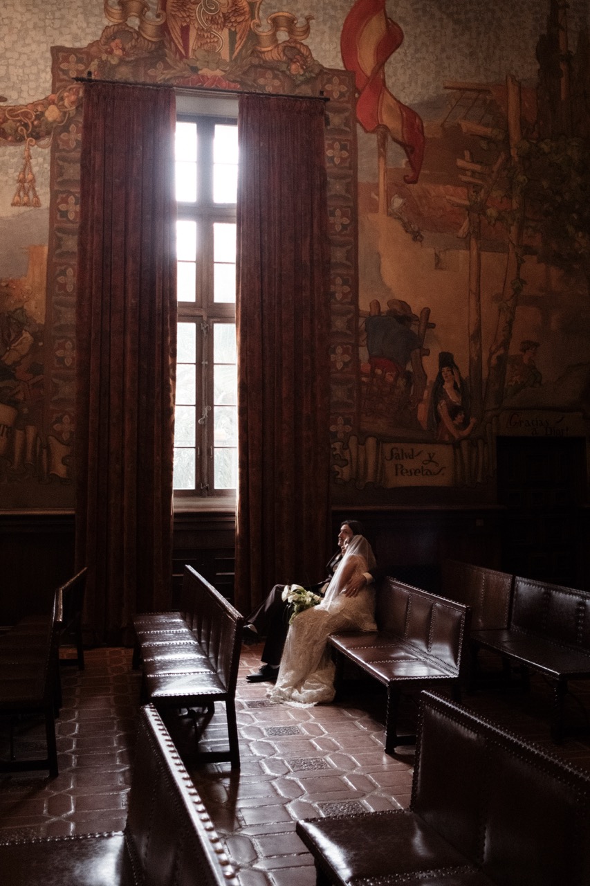 Person sitting on a bench in a dimly lit room with large window and ornate wall murals.