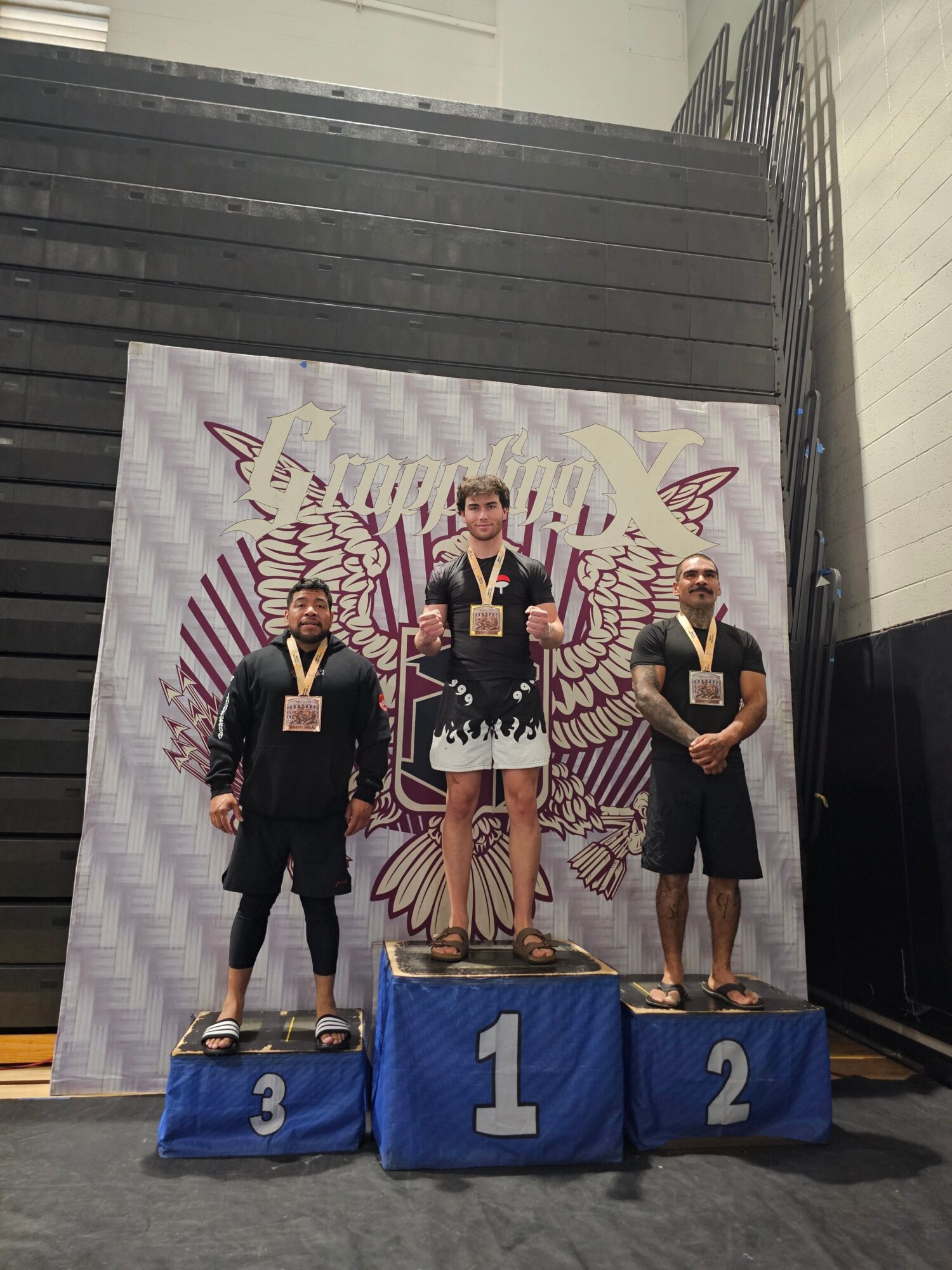 Three people stand on a winners' podium with medals, in front of a decorative backdrop featuring a butterfly design.