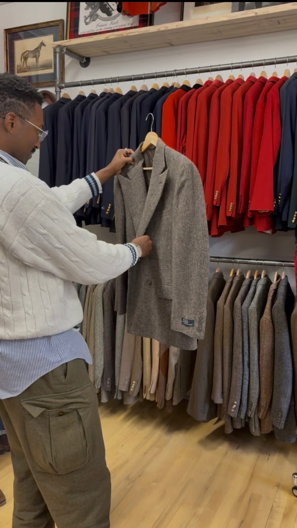 Person shopping for coats in a clothing store, browsing gray and red jackets on racks, wooden floor visible.