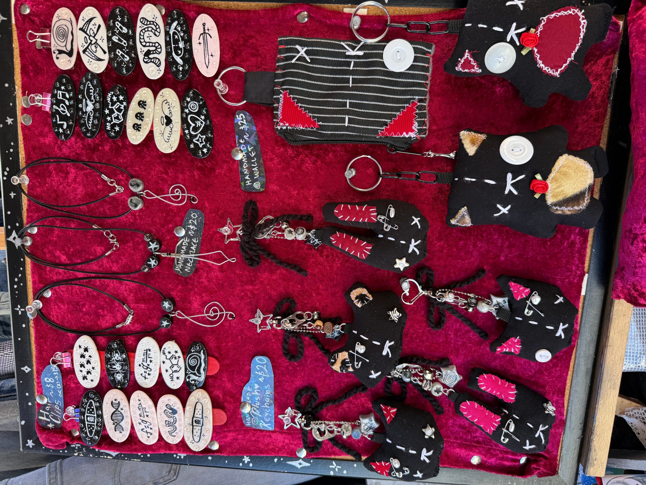 Display of various jewelry and accessories on a red fabric background, including rings, necklaces, and keychains with black, white, and red designs.