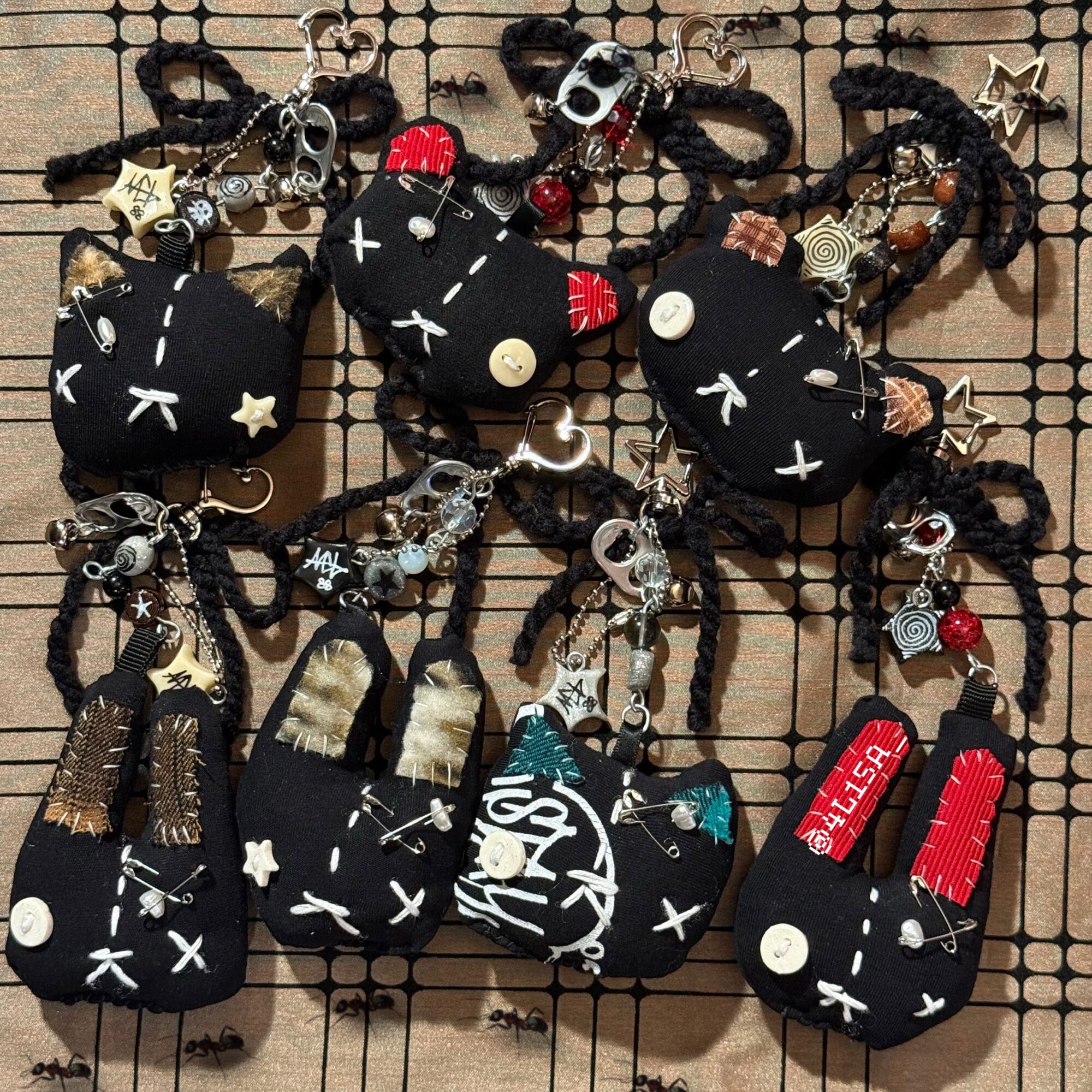 Collection of black plush keychains with various accessories and designs, displayed on a grid surface.