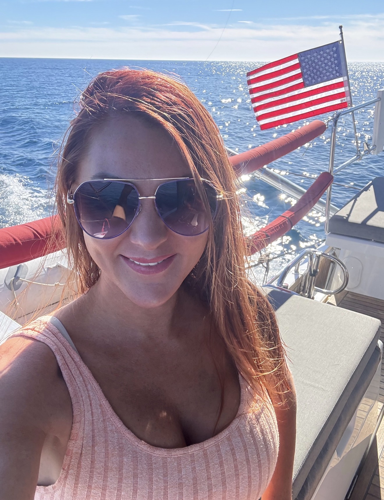 Woman with sunglasses smiling on boat with American flag and ocean background.