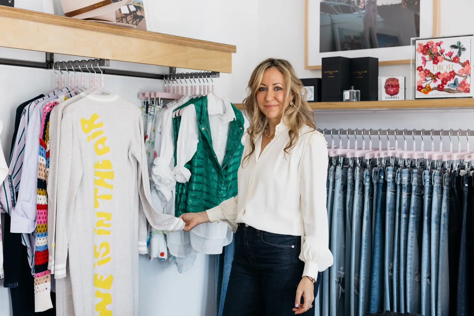 Woman shopping for clothes in a store, holding a white shirt, surrounded by hanging garments and shelves.