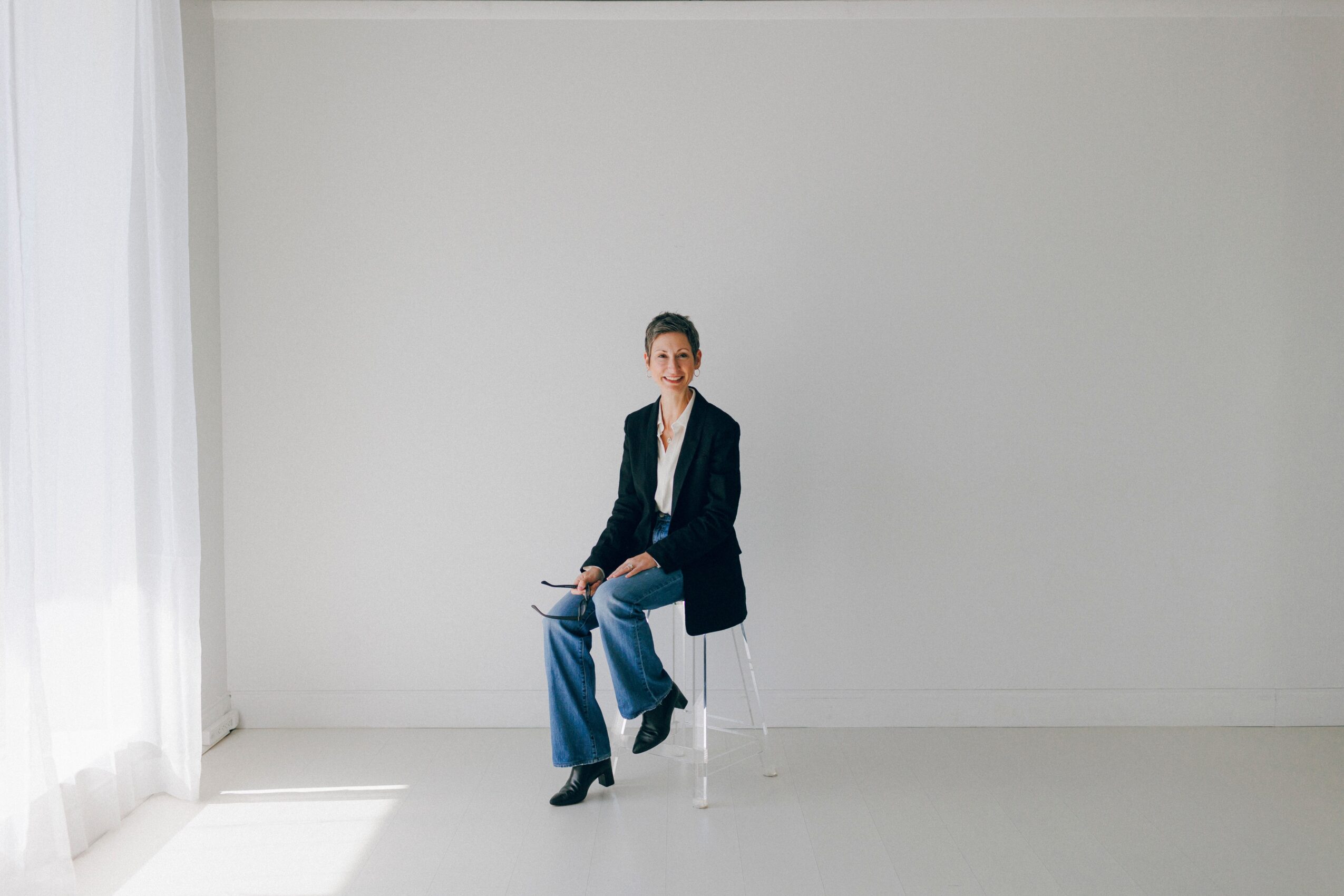 Person sitting on a white chair in a bright room with white walls and curtains.