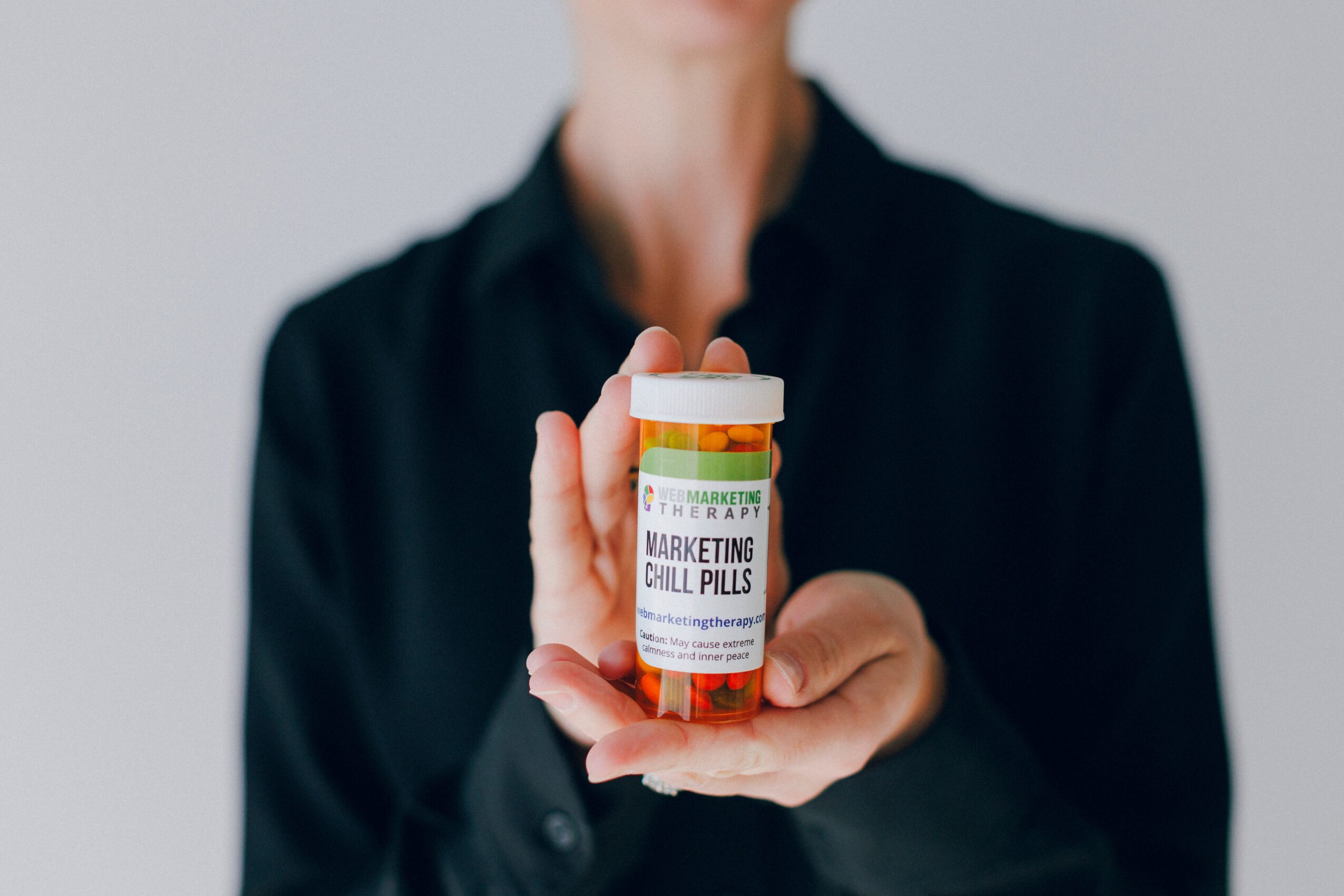 Person holding a bottle labeled 'Marketing Coll Pills' with a blurred background.