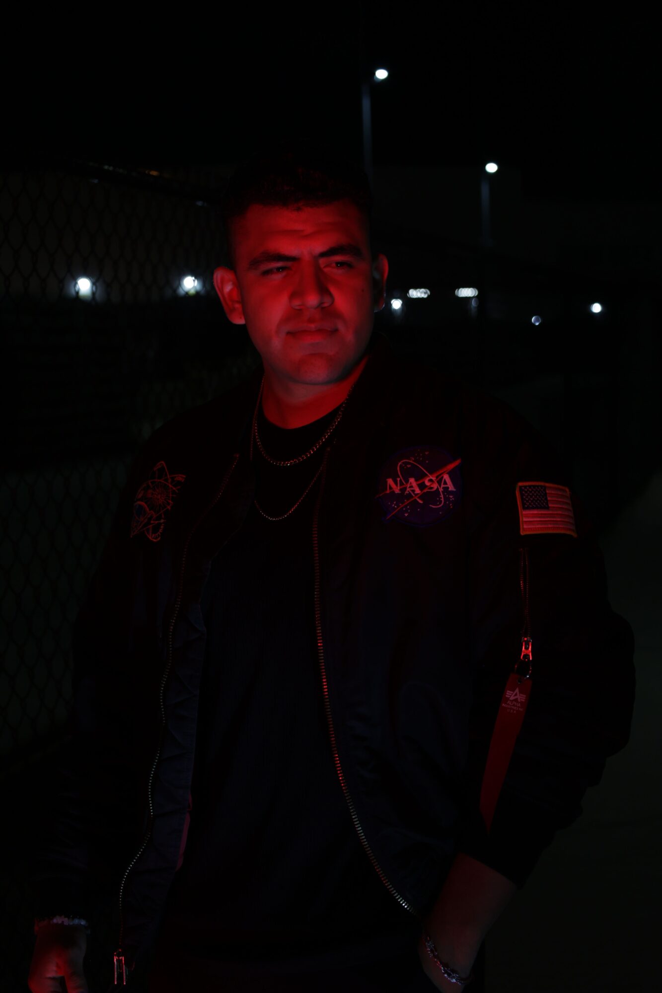 Person with red lighting on face, dark background, wearing dark clothing, in a dimly lit environment.