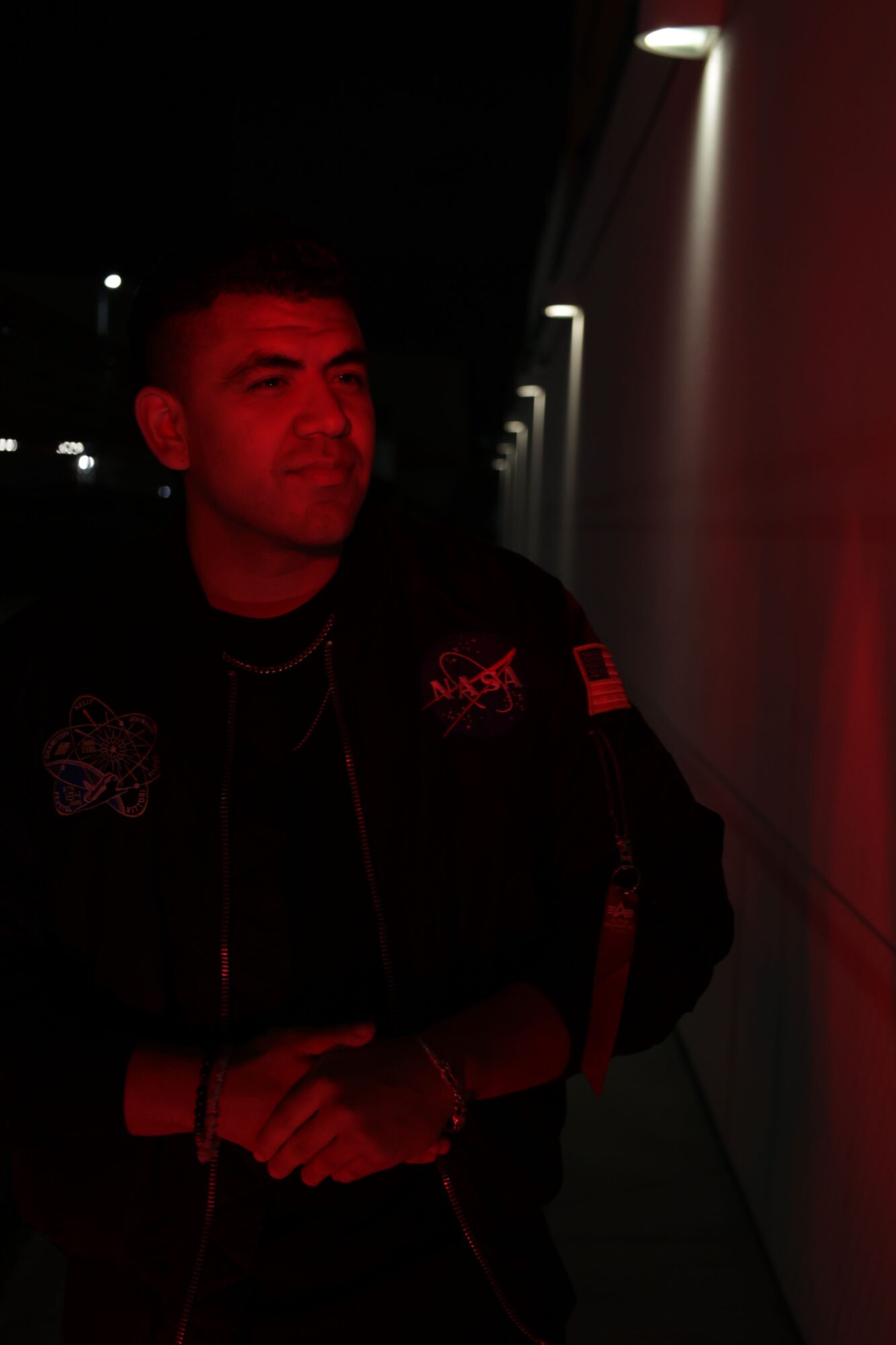Person standing in a dark corridor with illuminated floor lights, arms crossed, face partially visible, wearing dark clothing.