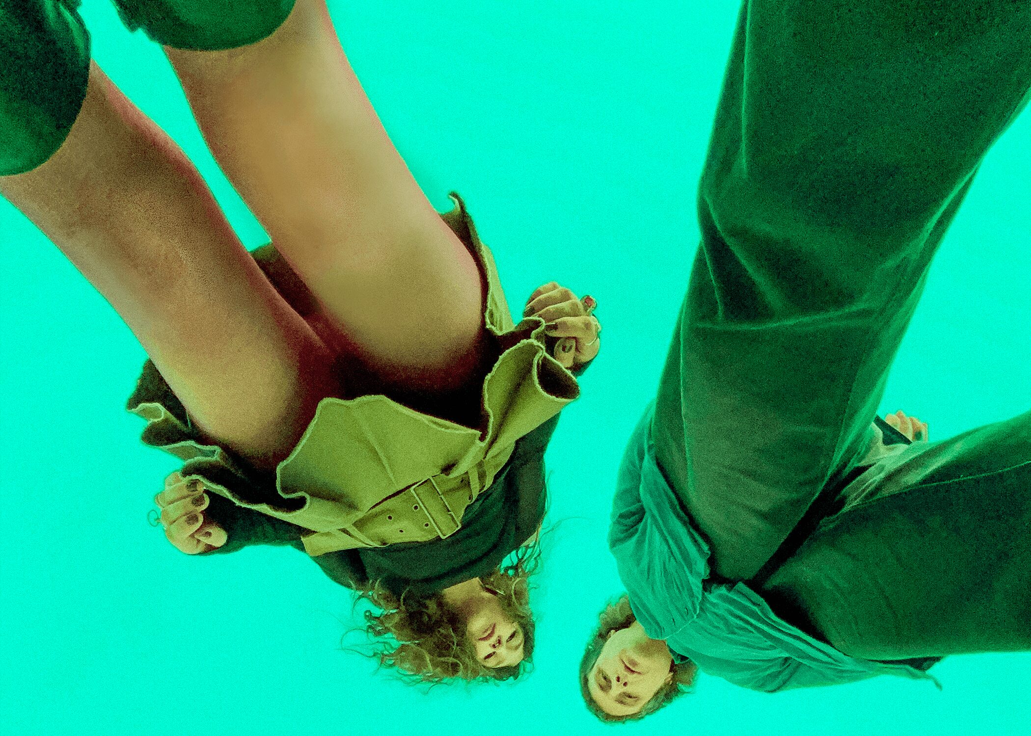 Two children lying on a green surface, one upside down and the other upright, with their heads close together.