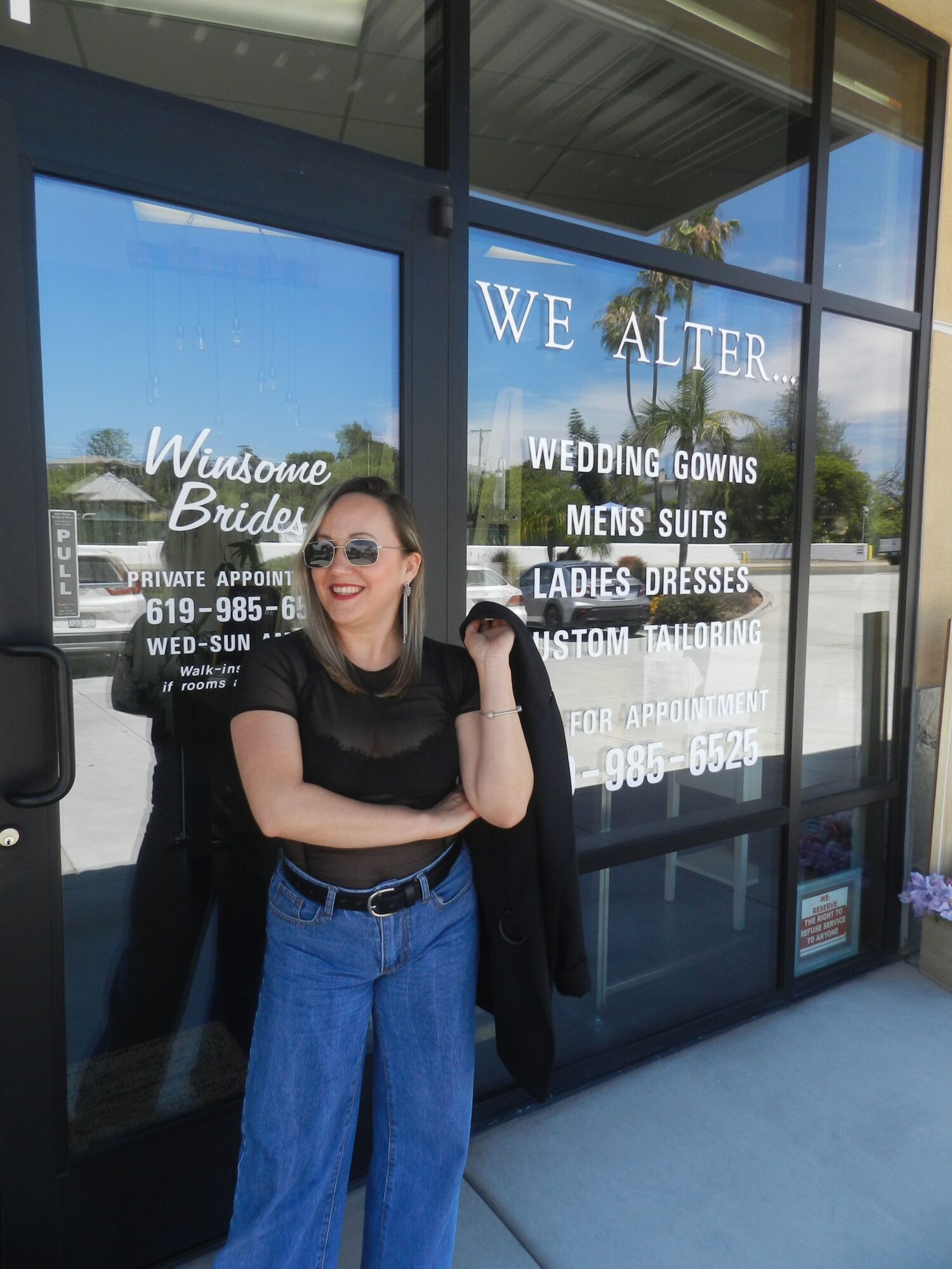 Woman standing at bus stop with glass panels, advertising water filter, and blue sky reflected in glass.