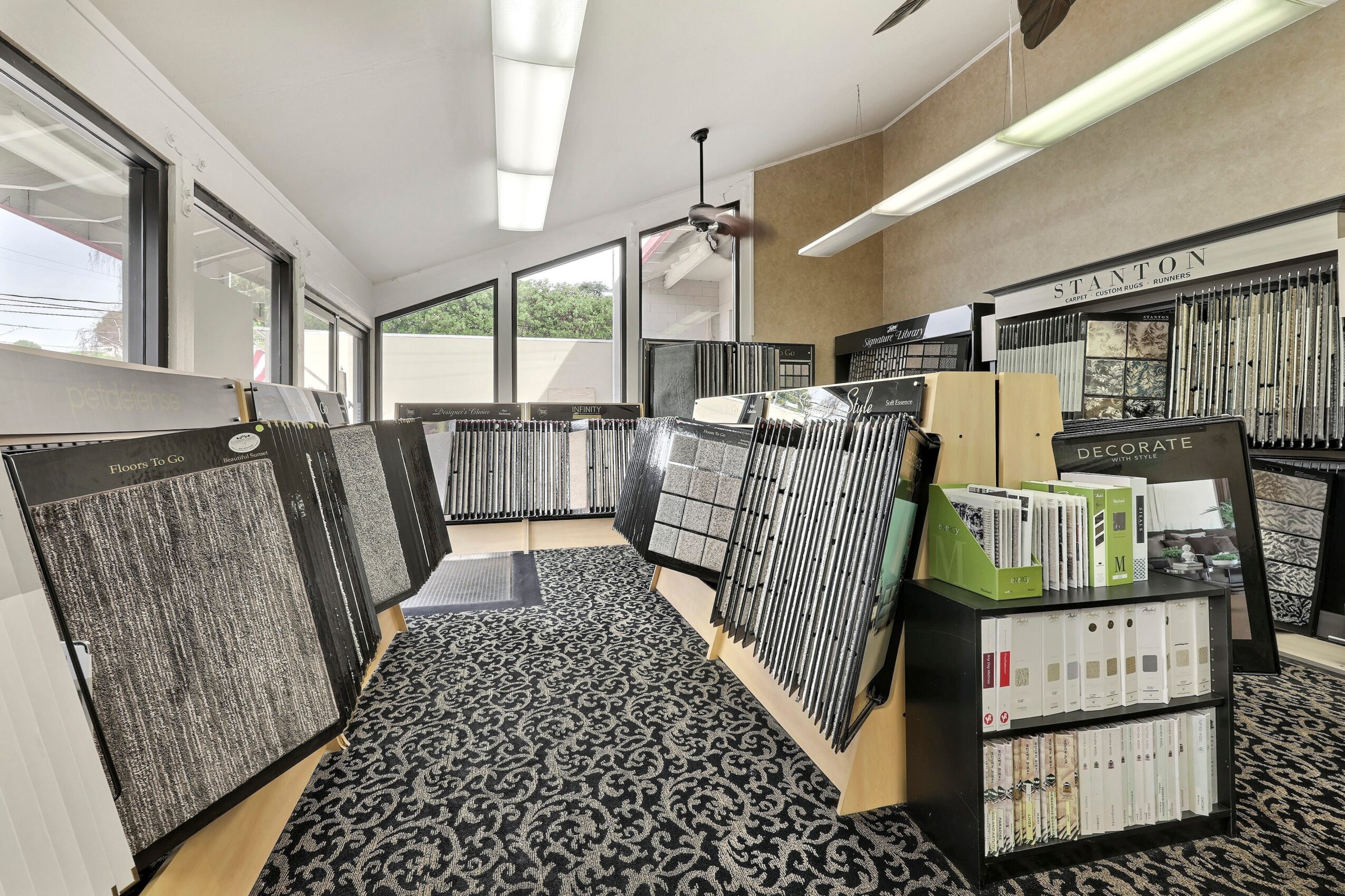Interior of a flooring store with carpet samples displayed on racks and a patterned carpet runner on the floor.