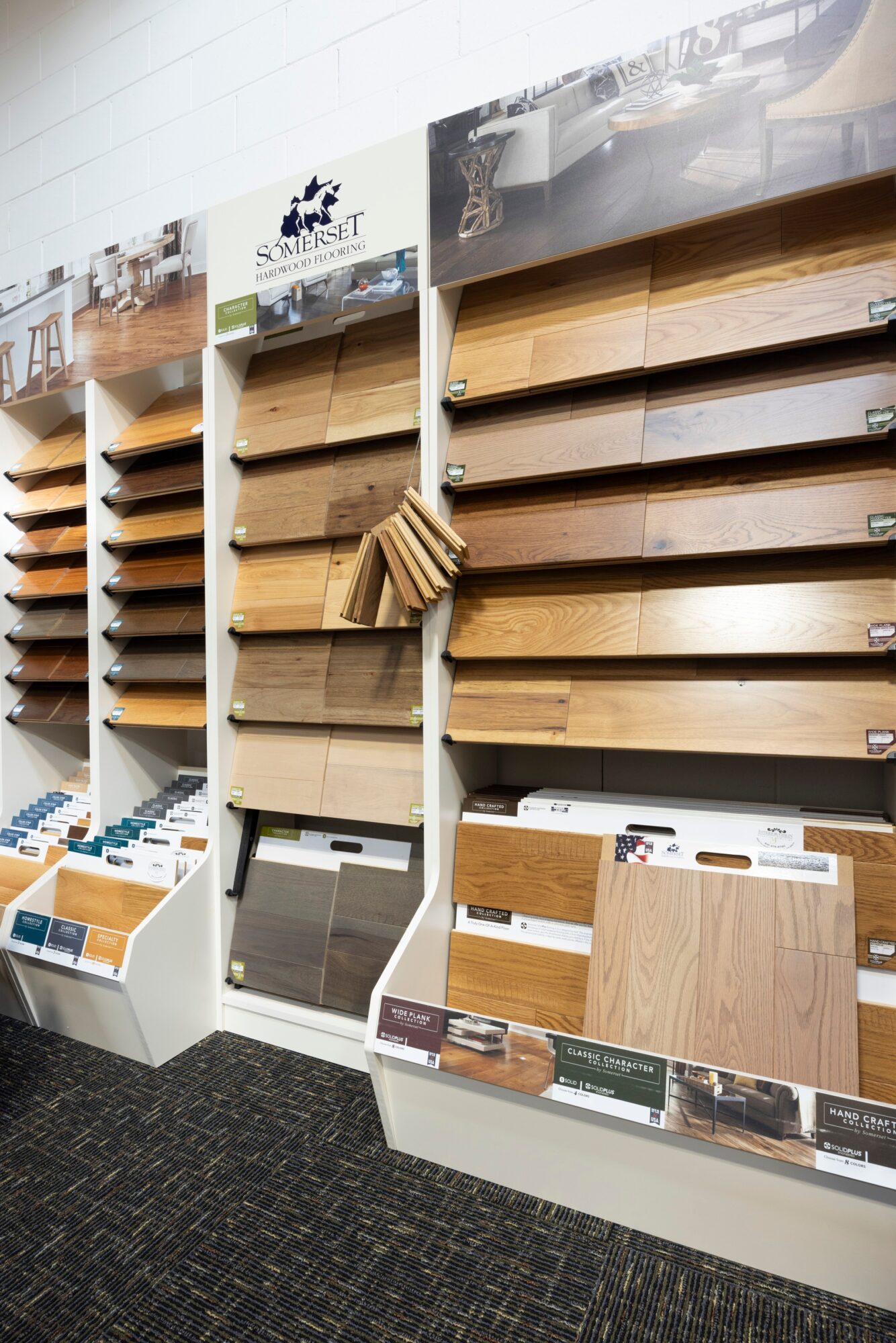Display of wooden flooring samples arranged on angled racks with sample swatches below, in a store setting.