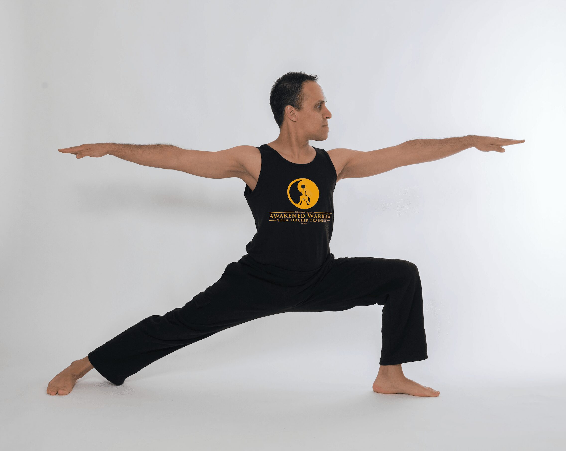 Person in a yoga pose with arms extended, legs apart, wearing a black tank top and pants, against a white background.