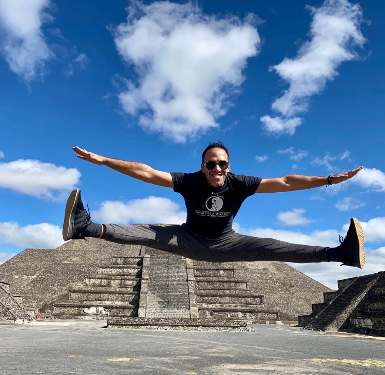 Person performing a split jump outdoors with stairs and blue sky with clouds in background