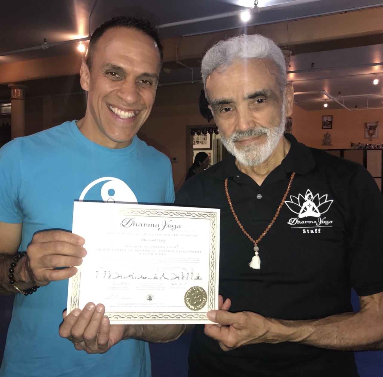 Two men holding a certificate, smiling, in an indoor setting with warm lighting.