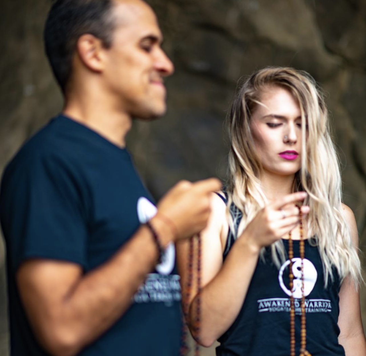 Two people outdoors, one man in a dark shirt and a woman with long blonde hair, both looking at their phones.